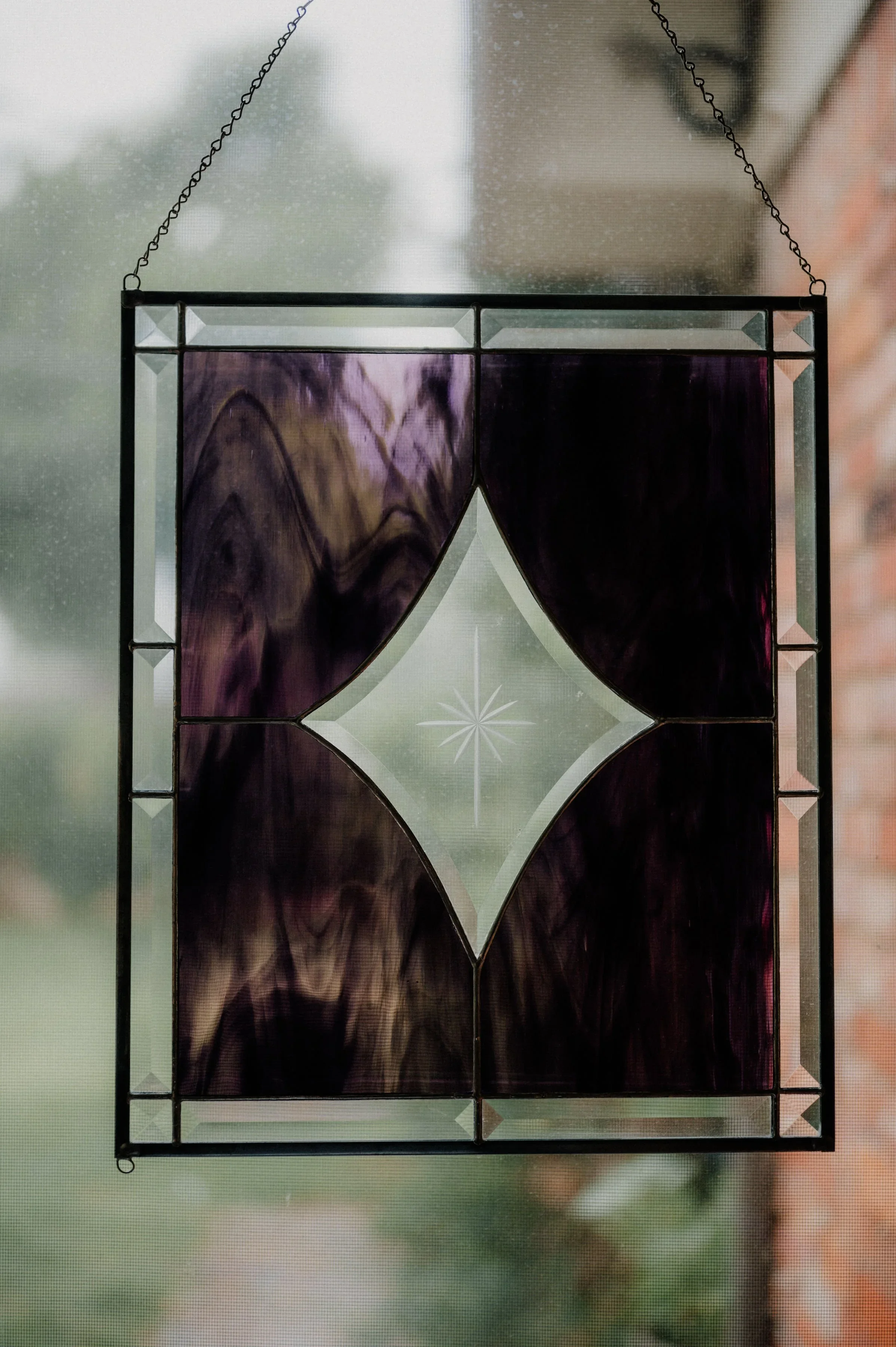 Stained glass hanging panel with purple and clear sections, suspended by chains near a window.