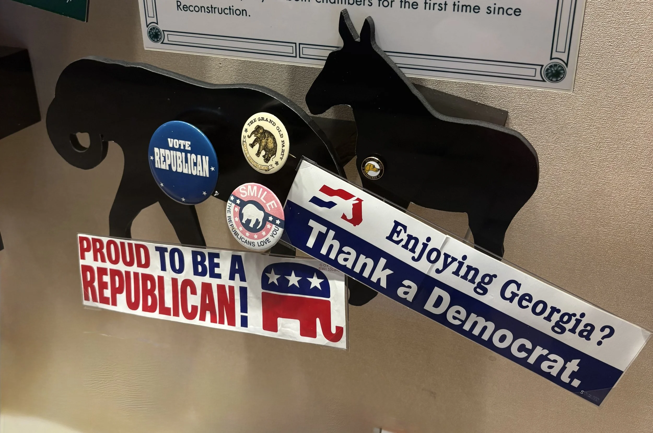 A wooden ballot box with the words 'BALLOT BOX' on the top and 'BEN HILL COUNTY' on the front, behind a glass display case.