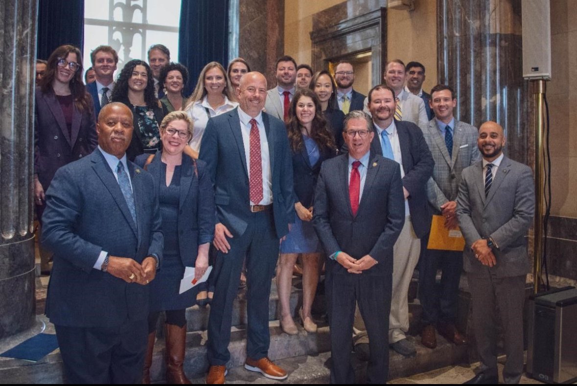 Group of professionally dressed people posing together in a formal setting, possibly a conference or event.
