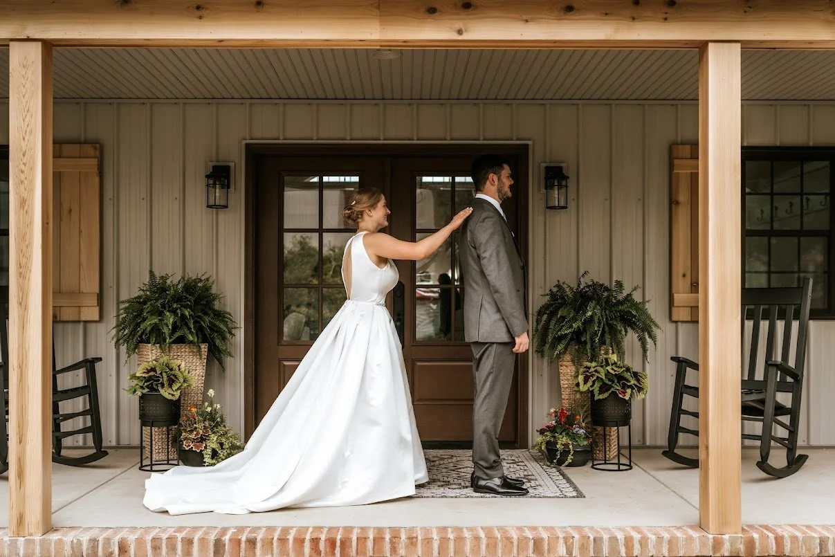 Bride touching groom's shoulder on a porch with houseplants, rocking chairs, and windows