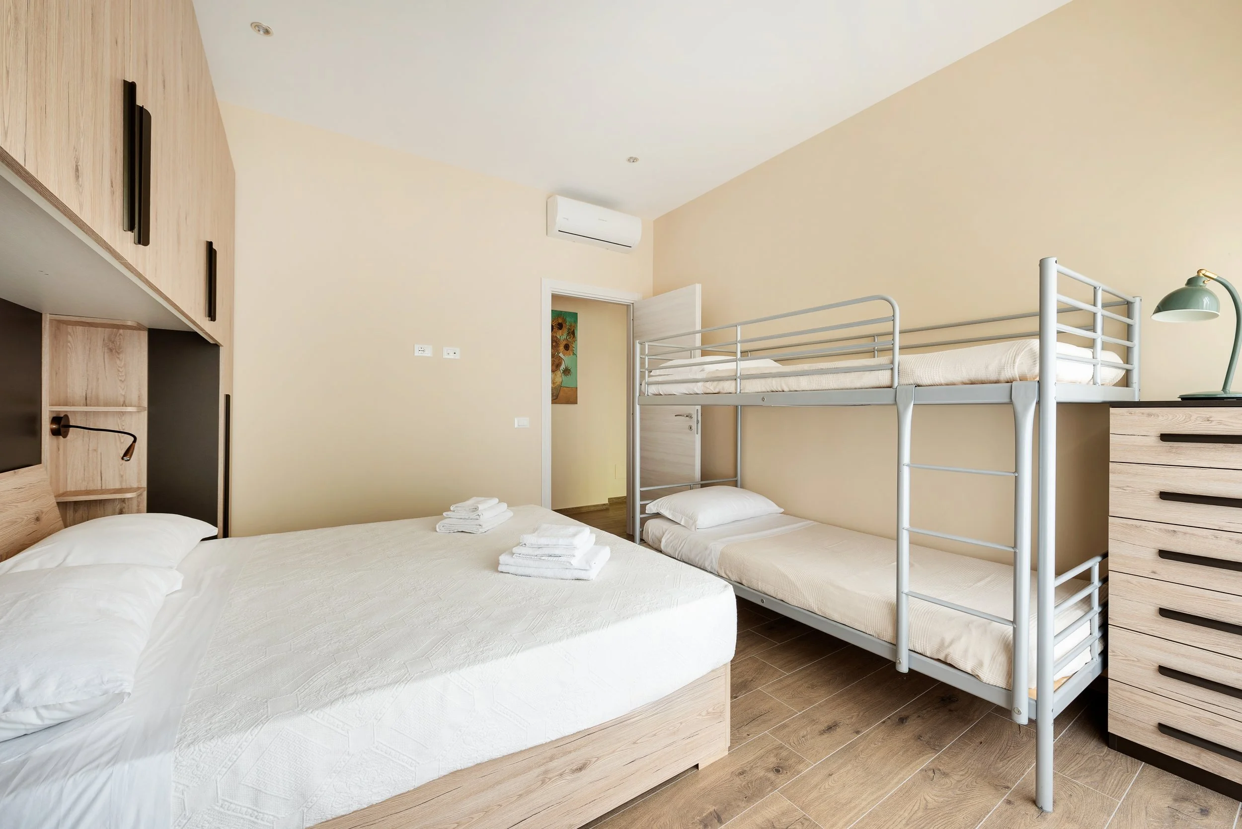 A bedroom with a large bed, a bunk bed, and wooden furniture in a modern, minimal style.