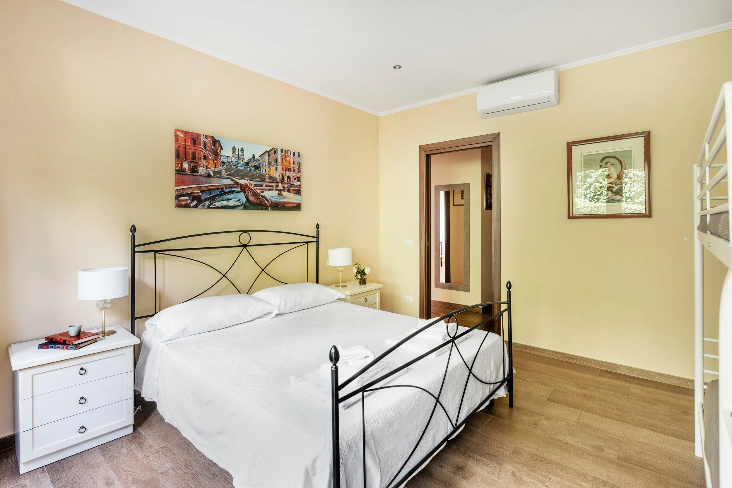 Bedroom with a metal bed, white bedding, nightstands with lamps, decorative wall art, a doorway, and wood flooring.