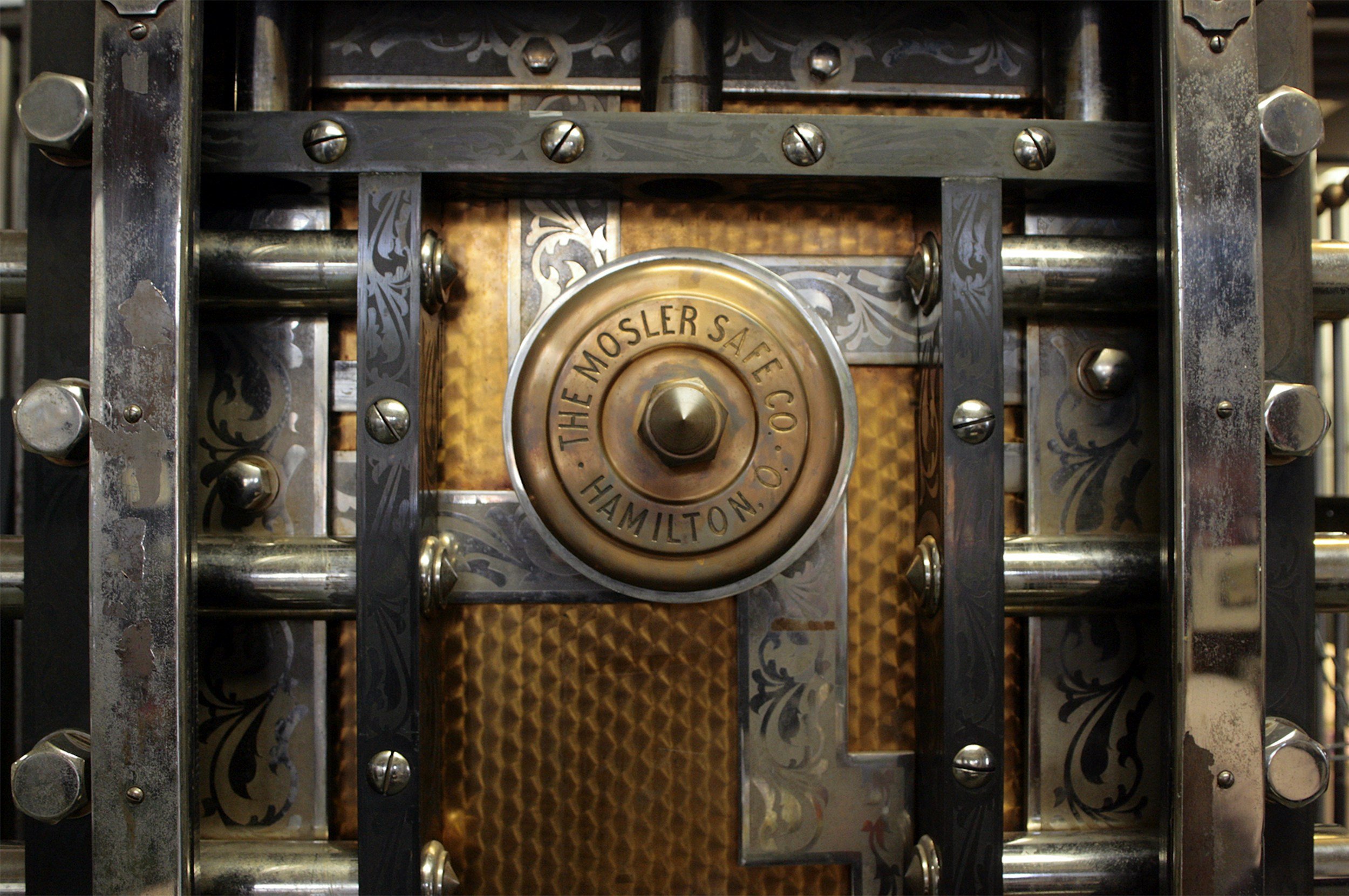 Close-up of an ornate vintage safe door with a brass wheel labeled 'The Mosler Safe Co. Hamilton, O.' and decorative metallic details.