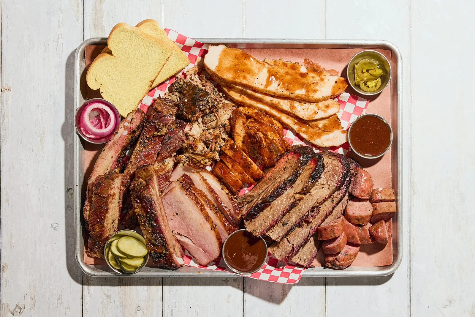 large platter of barbecue including 5 types of meat and small containers of sauces and sides