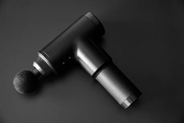 Black massage gun with a round attachment on a dark surface