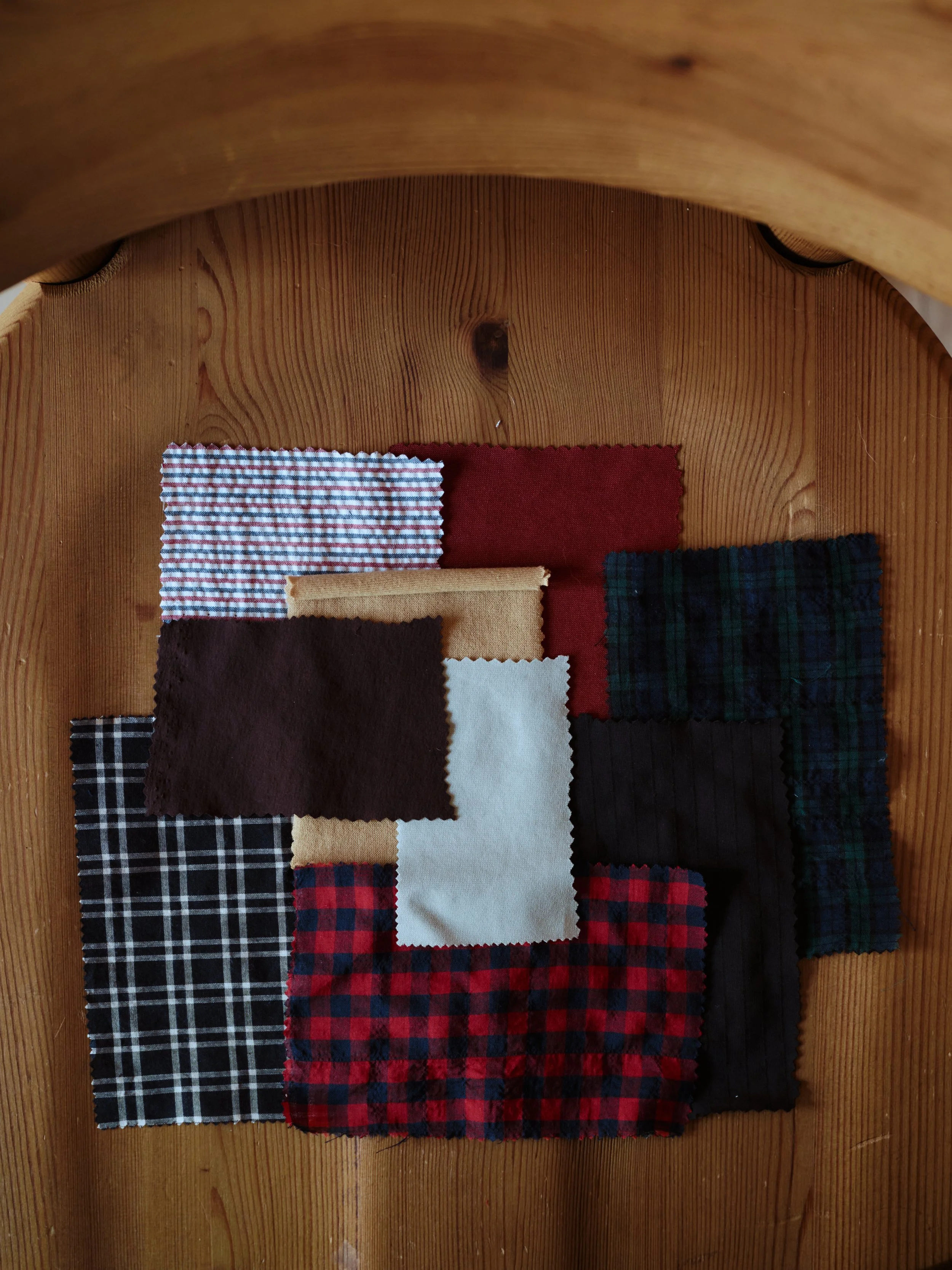 Various fabric swatches with different plaid and solid patterns, arranged on a wooden surface.