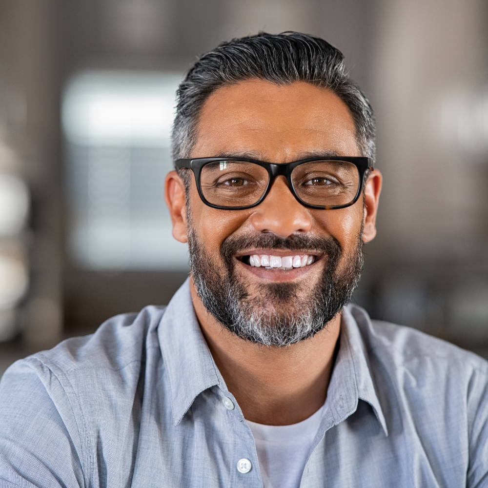 Close-up of smiling middle-aged man with glasses, beard, and gray hair in an indoor setting.