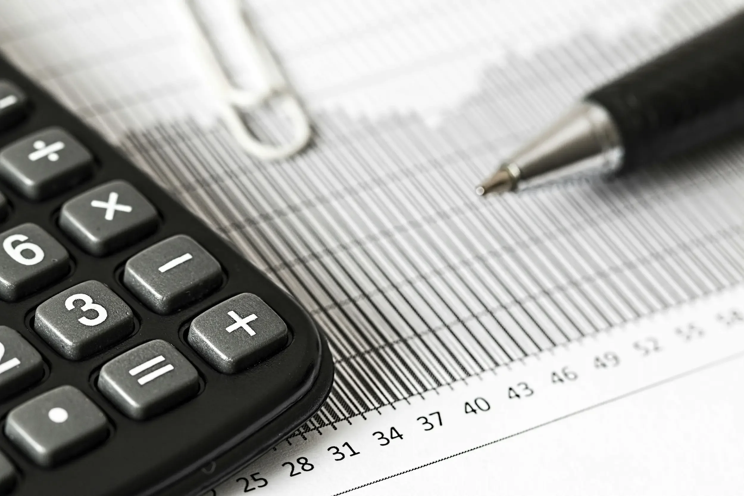 Close-up view of a calculator and a pen resting on sheet of paper with printed numbers and markings.