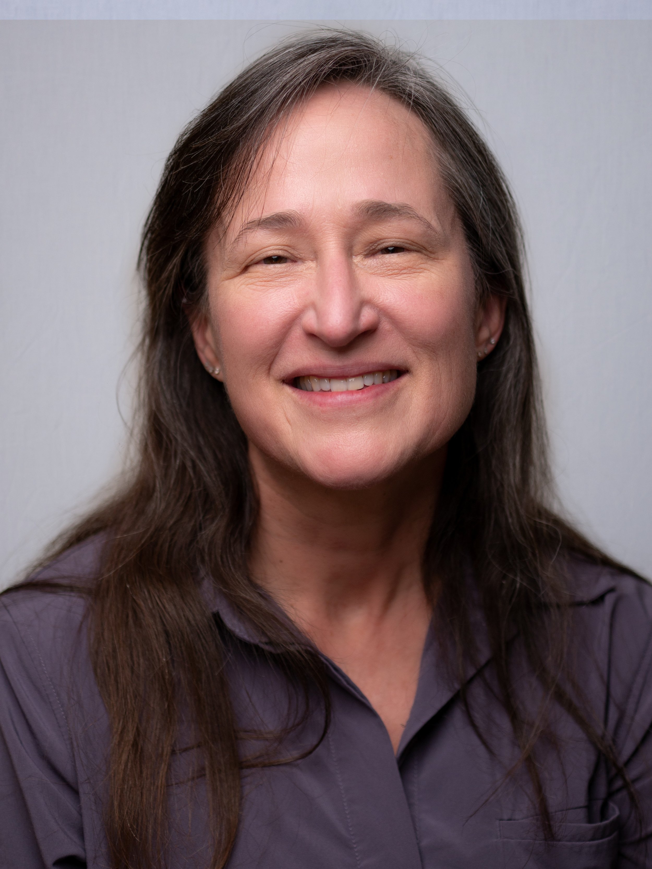 Dr. Cheryl Lewis, DNP (Dr. Lewis). Family Medicine and Primary Care in Bonney Lake, WA. A woman with long brown hair smiling at the camera, wearing a gray shirt, against a plain light gray background.