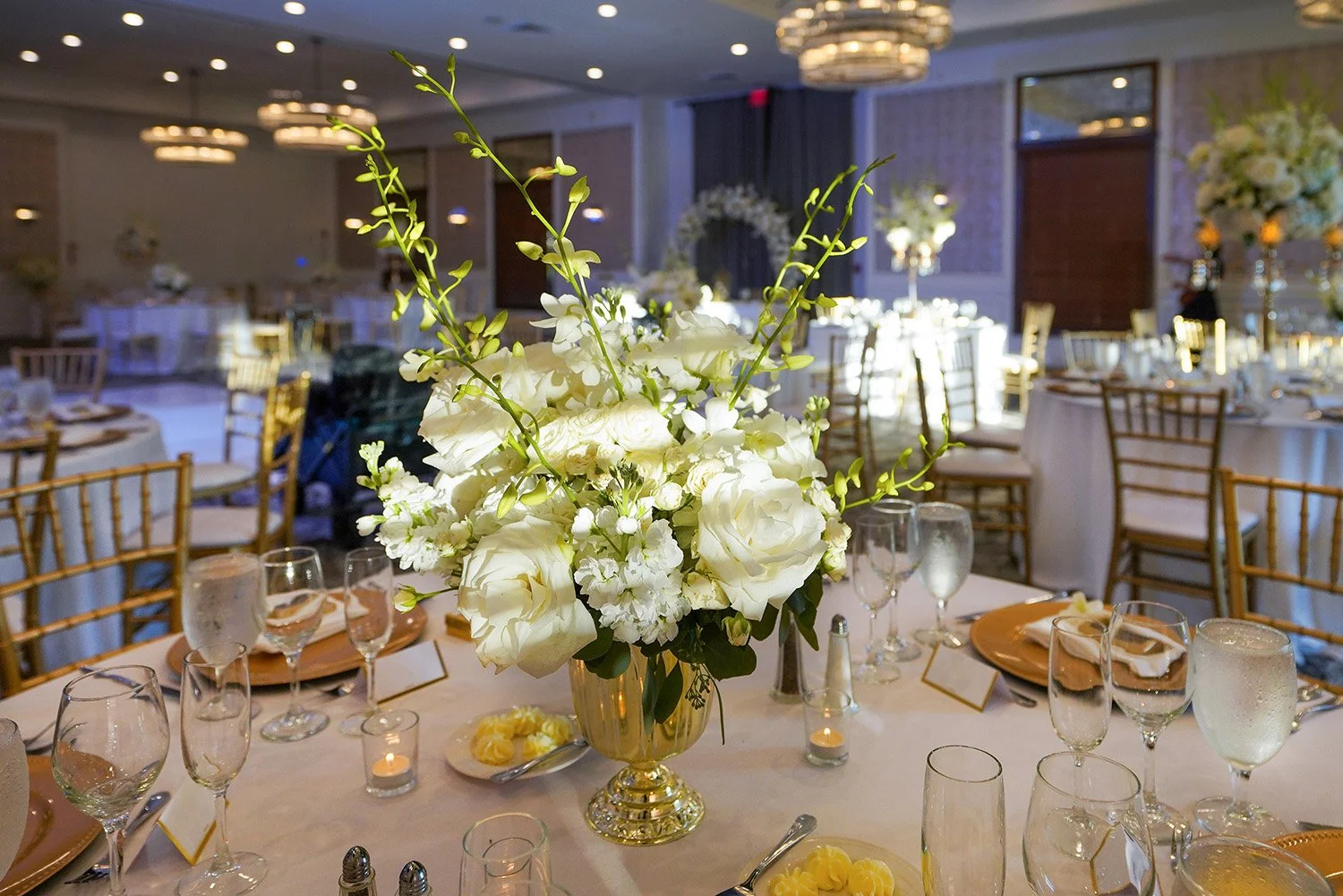 Formal indoor event setup, likely a wedding reception or gala, with a strong focus on a beautifully set guest table in the foreground.
