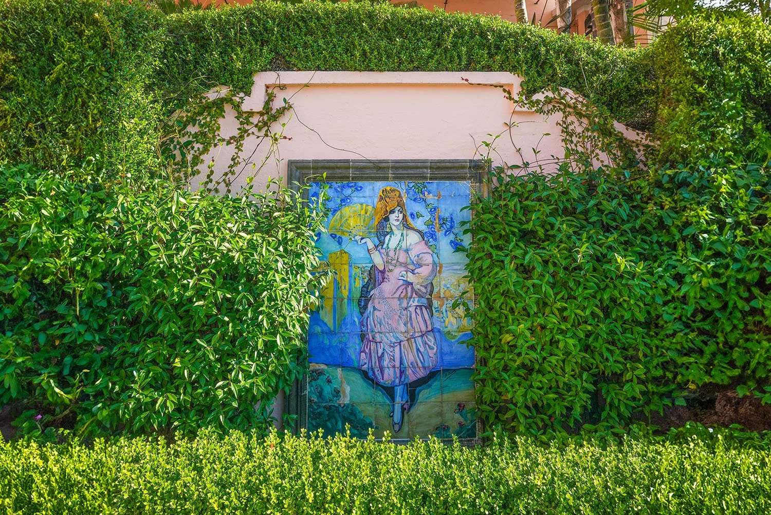 A five-tiered white wedding cake decorated with white roses and topped with a miniature bride and groom, displayed on a gold serving tray with surrounding candelabras and scattered white flower petals.