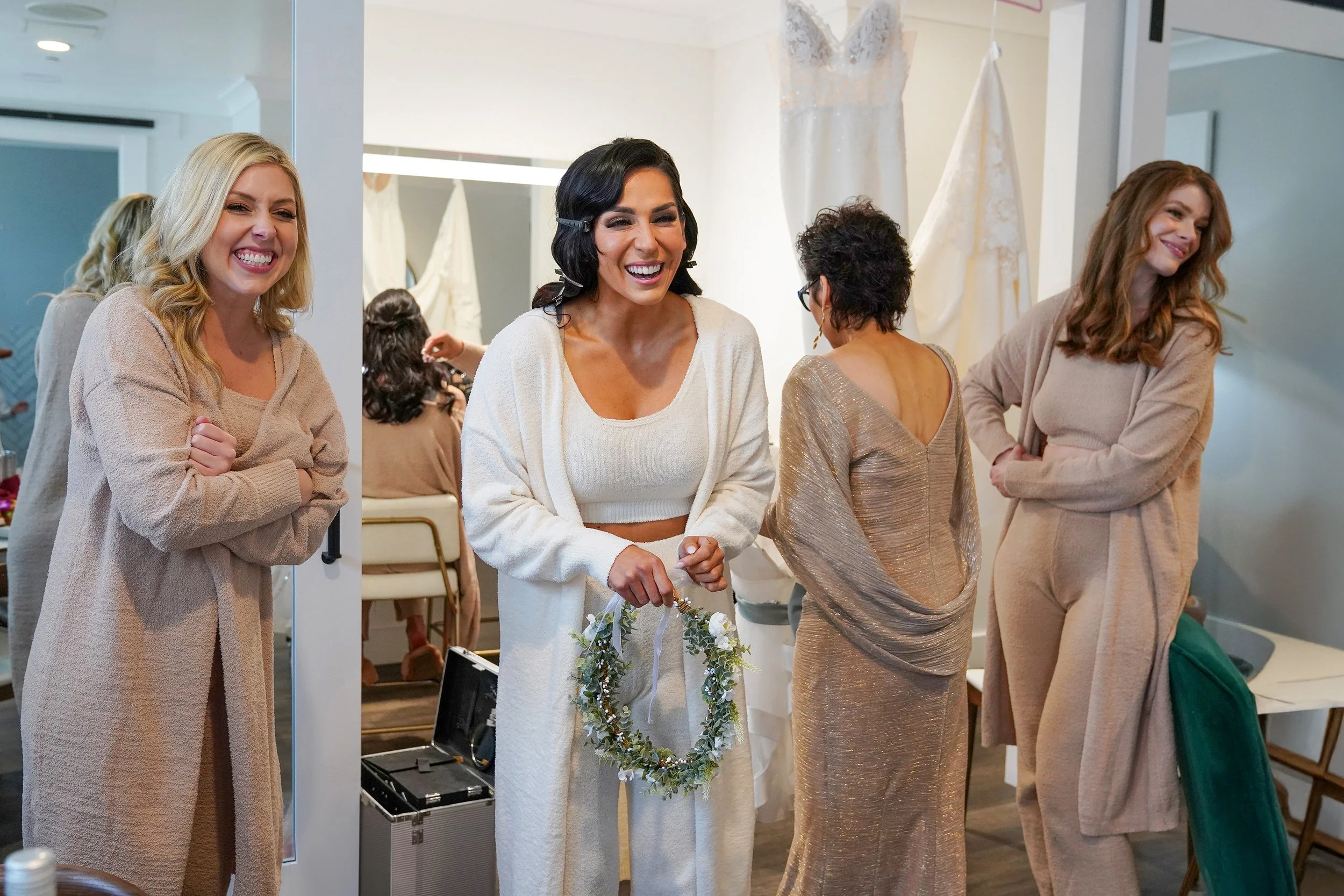Candid photo of a laughing bride and bridesmaids in matching lounge sets preparing for a wedding in a modern bridal suite.