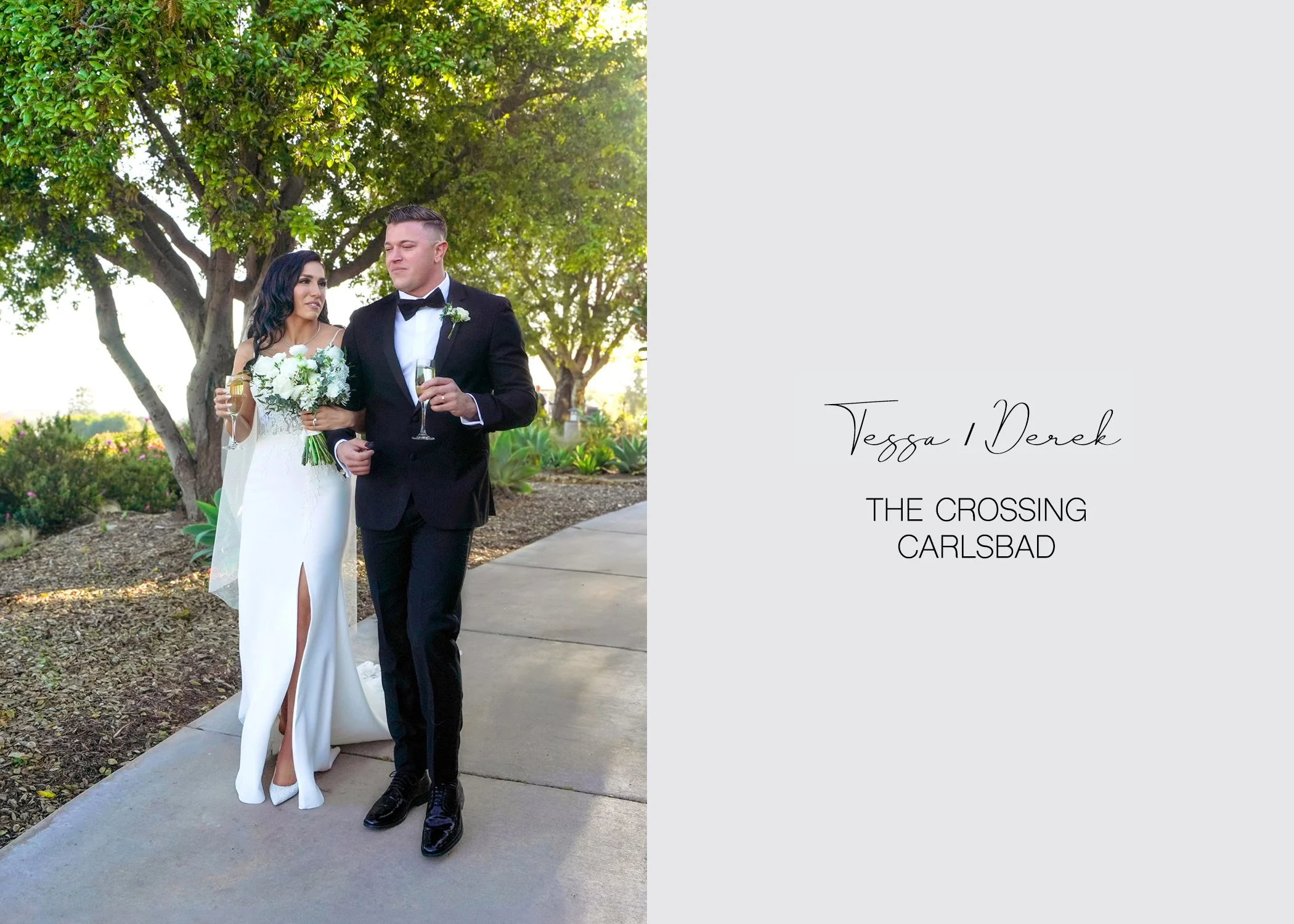 A newly married couple walks arm-in-arm along an outdoor pathway, each holding a champagne flute for a celebratory toast. The setting is lush with green trees and foliage in a sunlit, San Diego, California.
