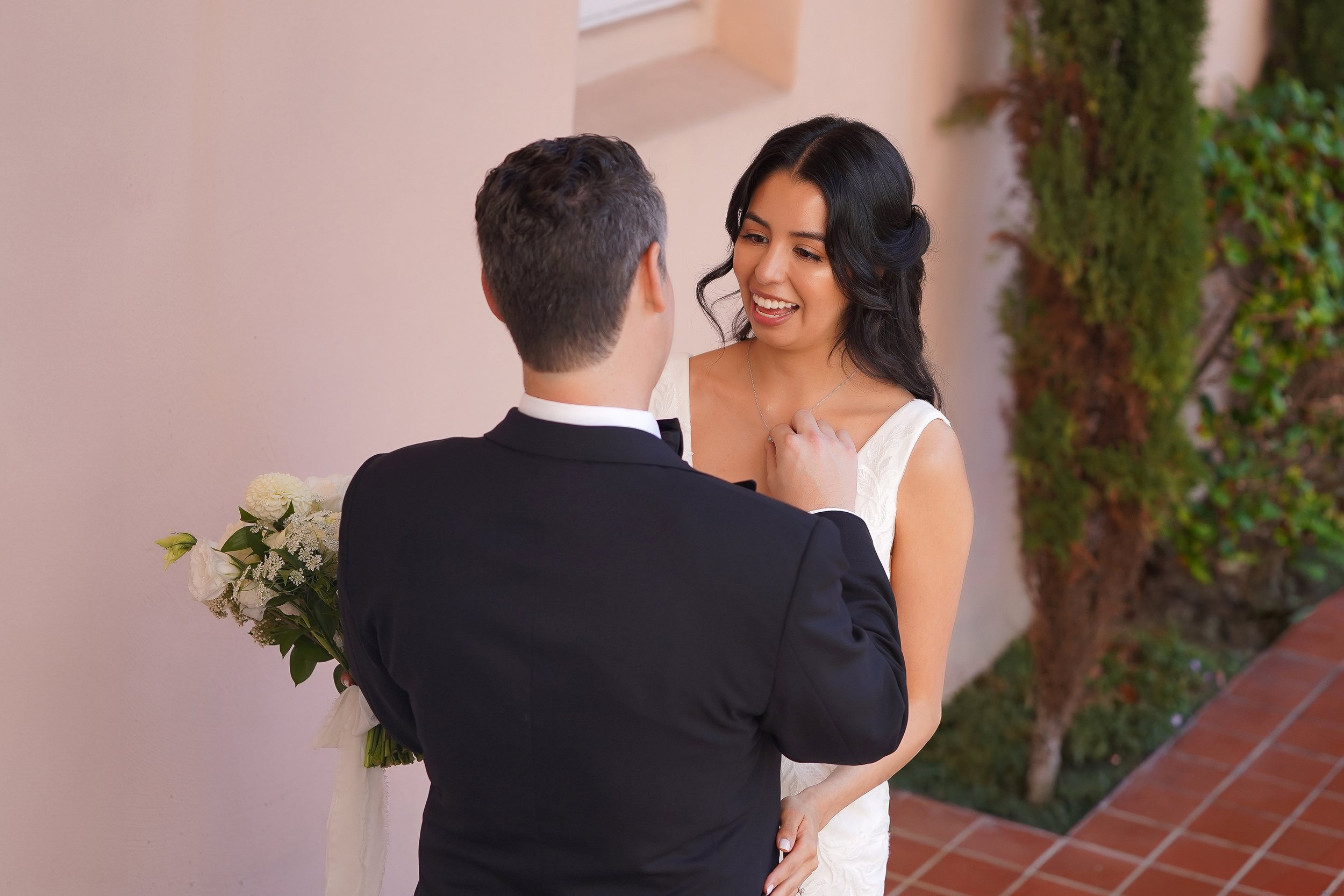 A bride in a white lace gown shows a joyful emotional reaction while looking at her groom during their wedding first look.