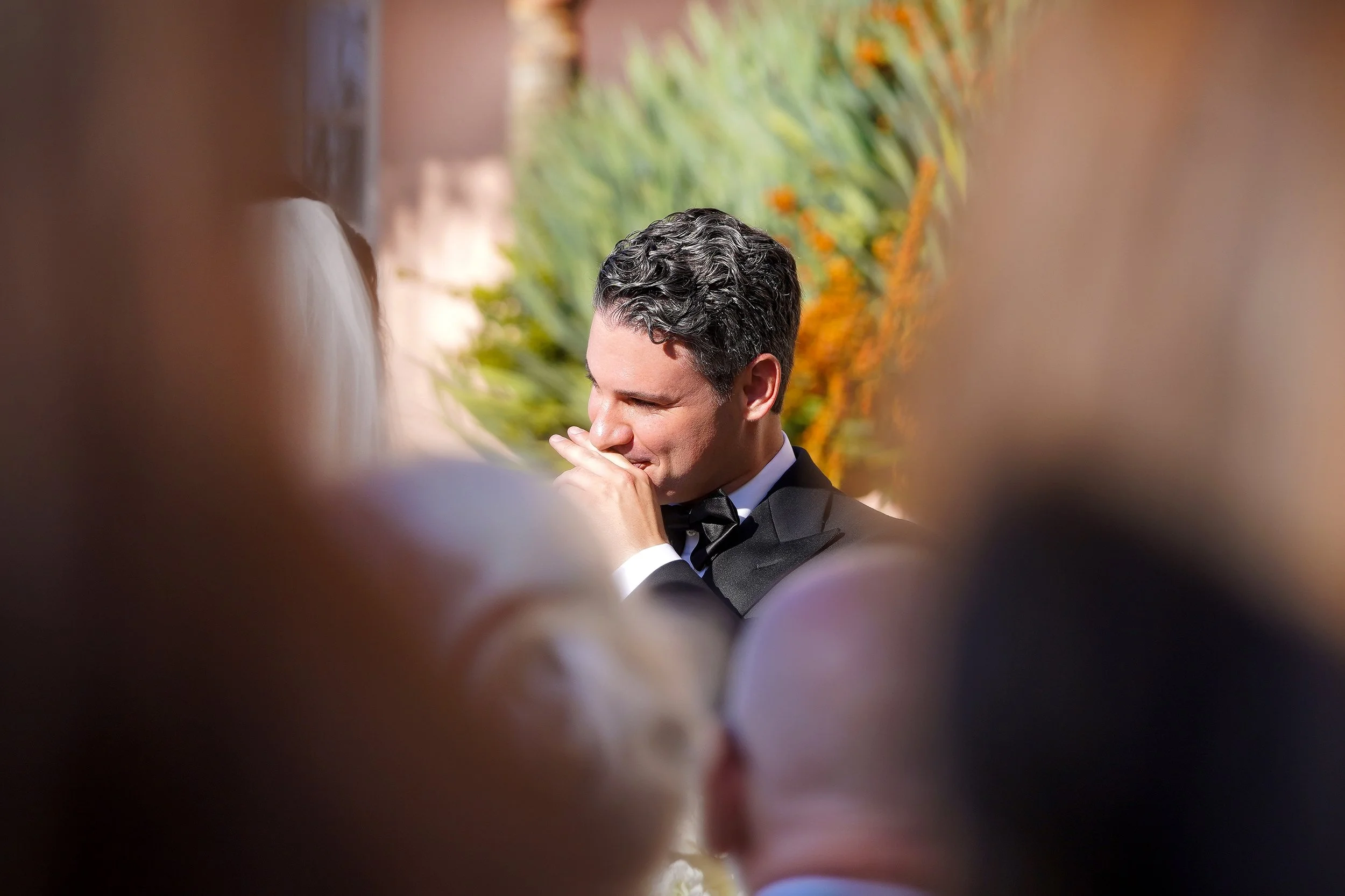 Groom in a black tuxedo having an emotional moment during an outdoor wedding ceremony.