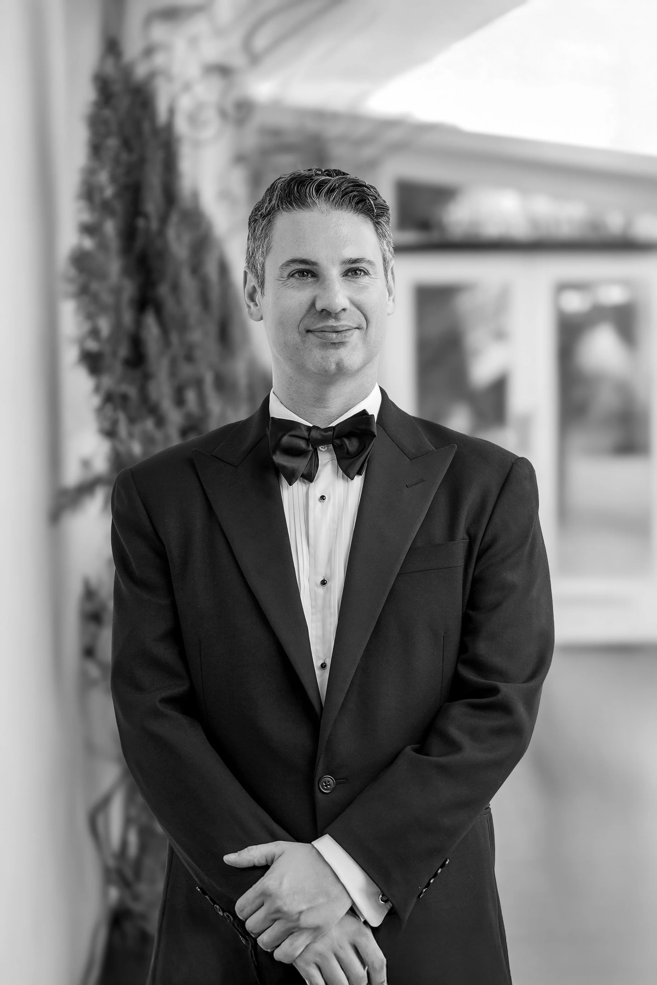 Formal black and white groom portrait featuring a traditional tuxedo with peak lapels.