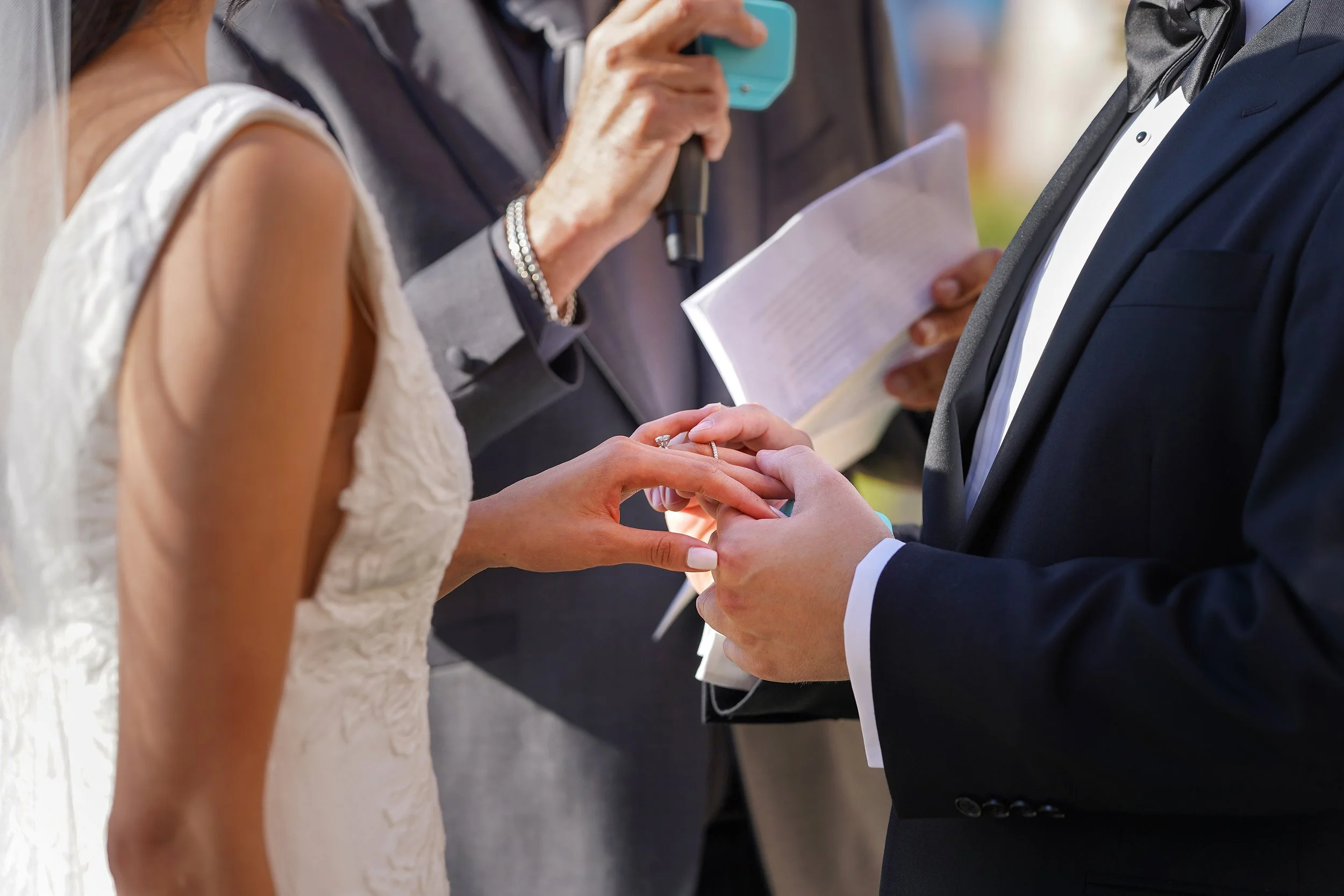 Wedding ring exchange between a bride and groom at an outdoor ceremony.