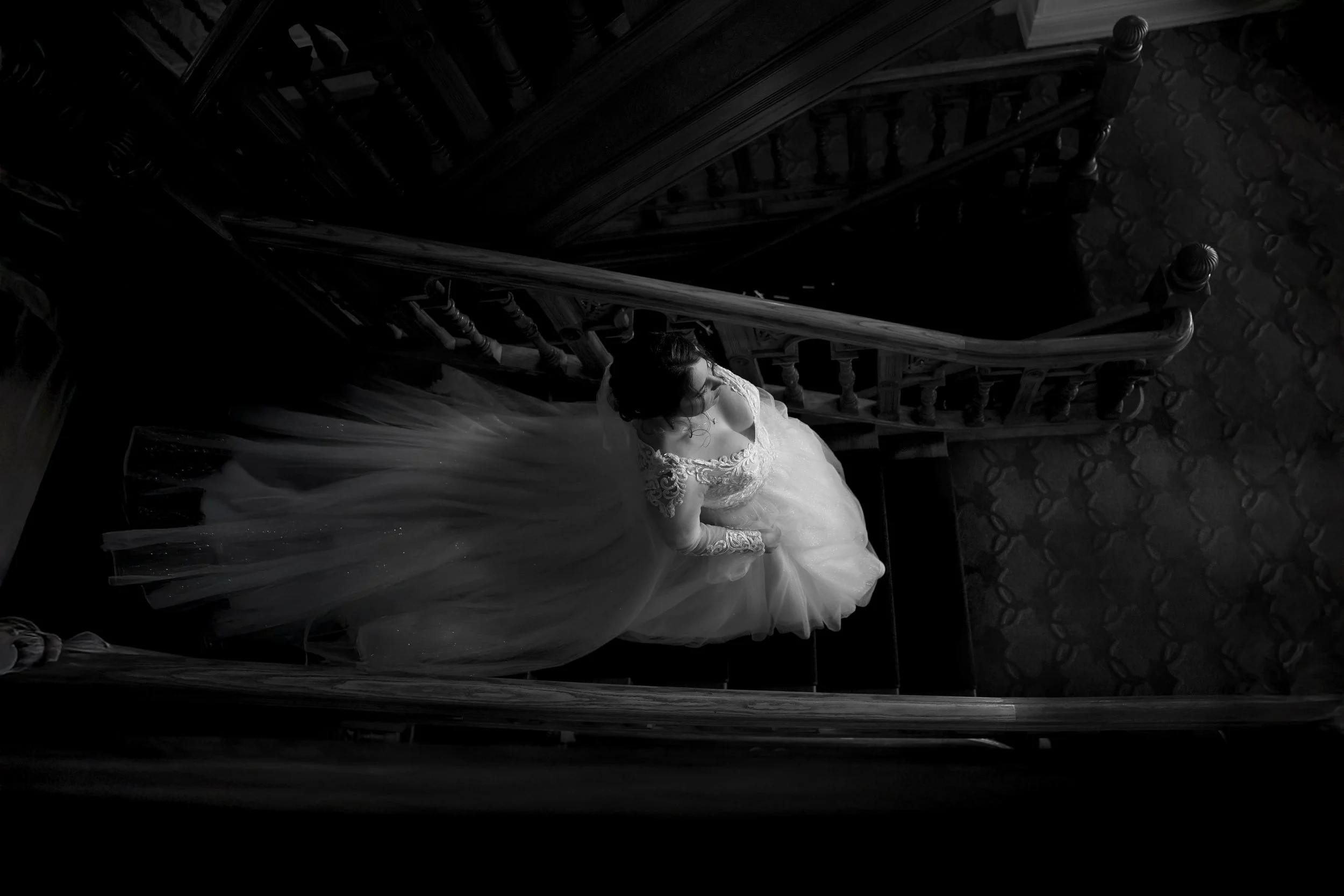 A woman in a wedding dress standing on a staircase seen from above in black and white.