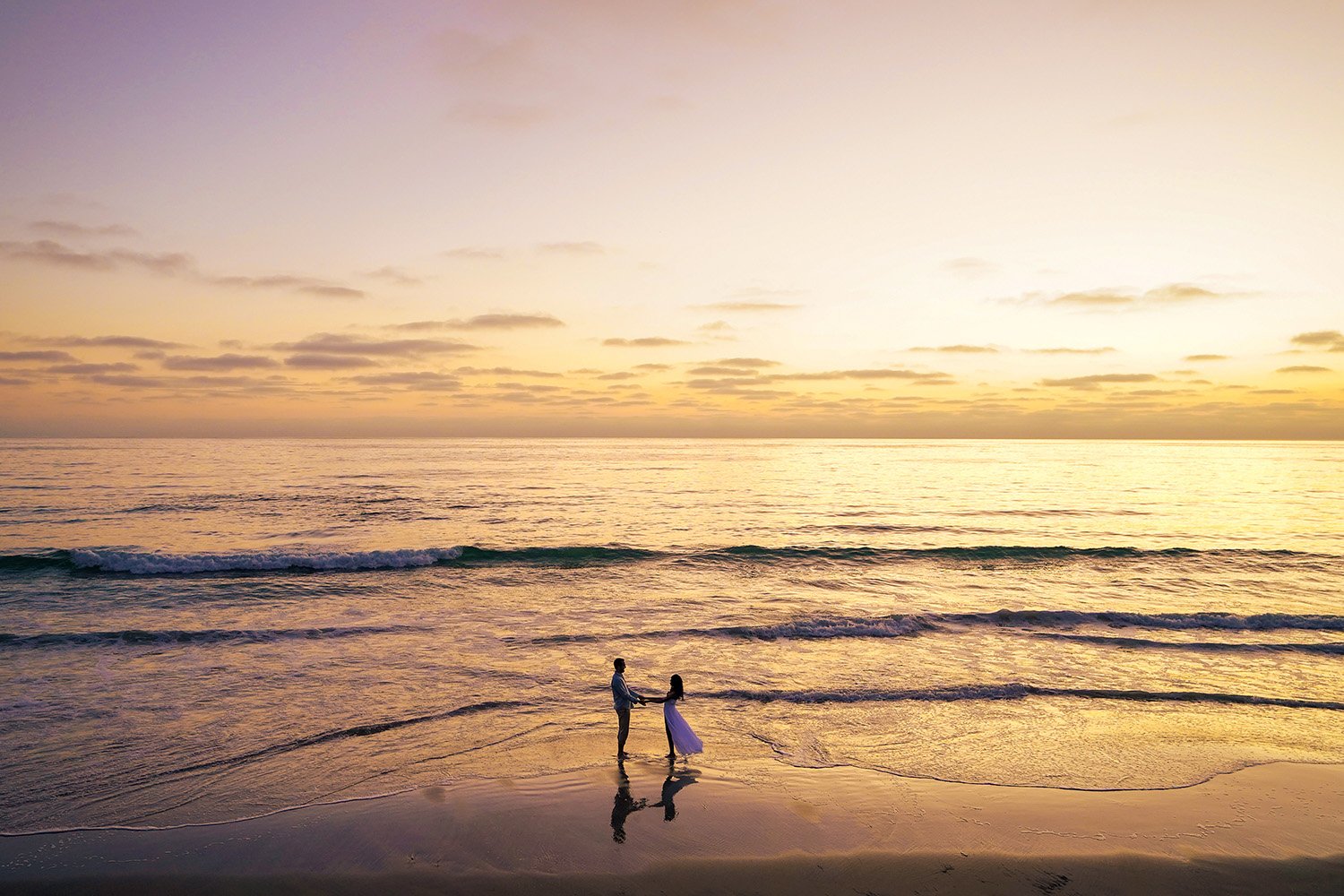 A couple holding hands and dancing in the shallow water at the beach during sunset.