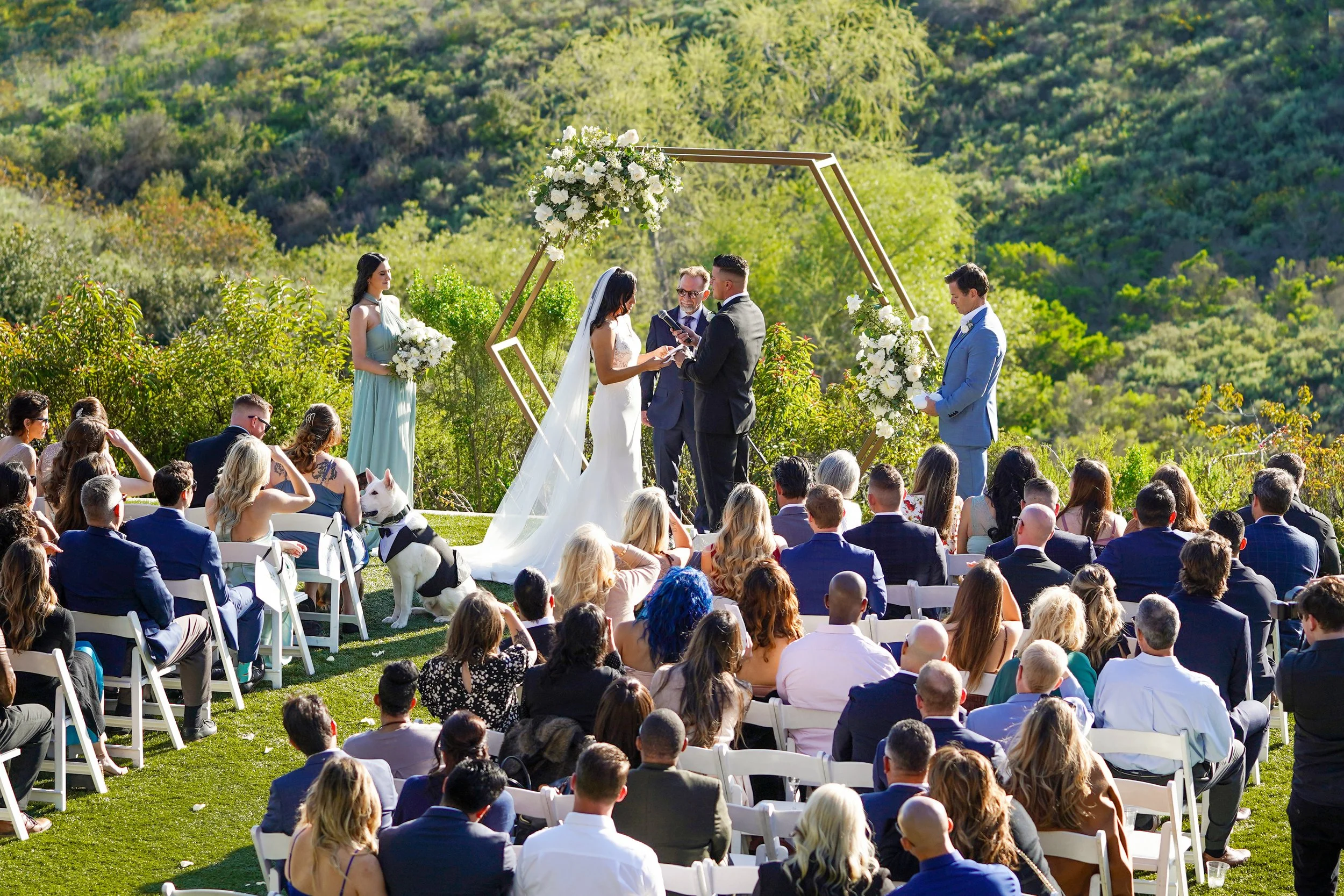 Hillside wedding ceremony at Serendipity Garden Weddings in Carlsbad, California, featuring a scenic mountain backdrop and floral hexagon arch."
