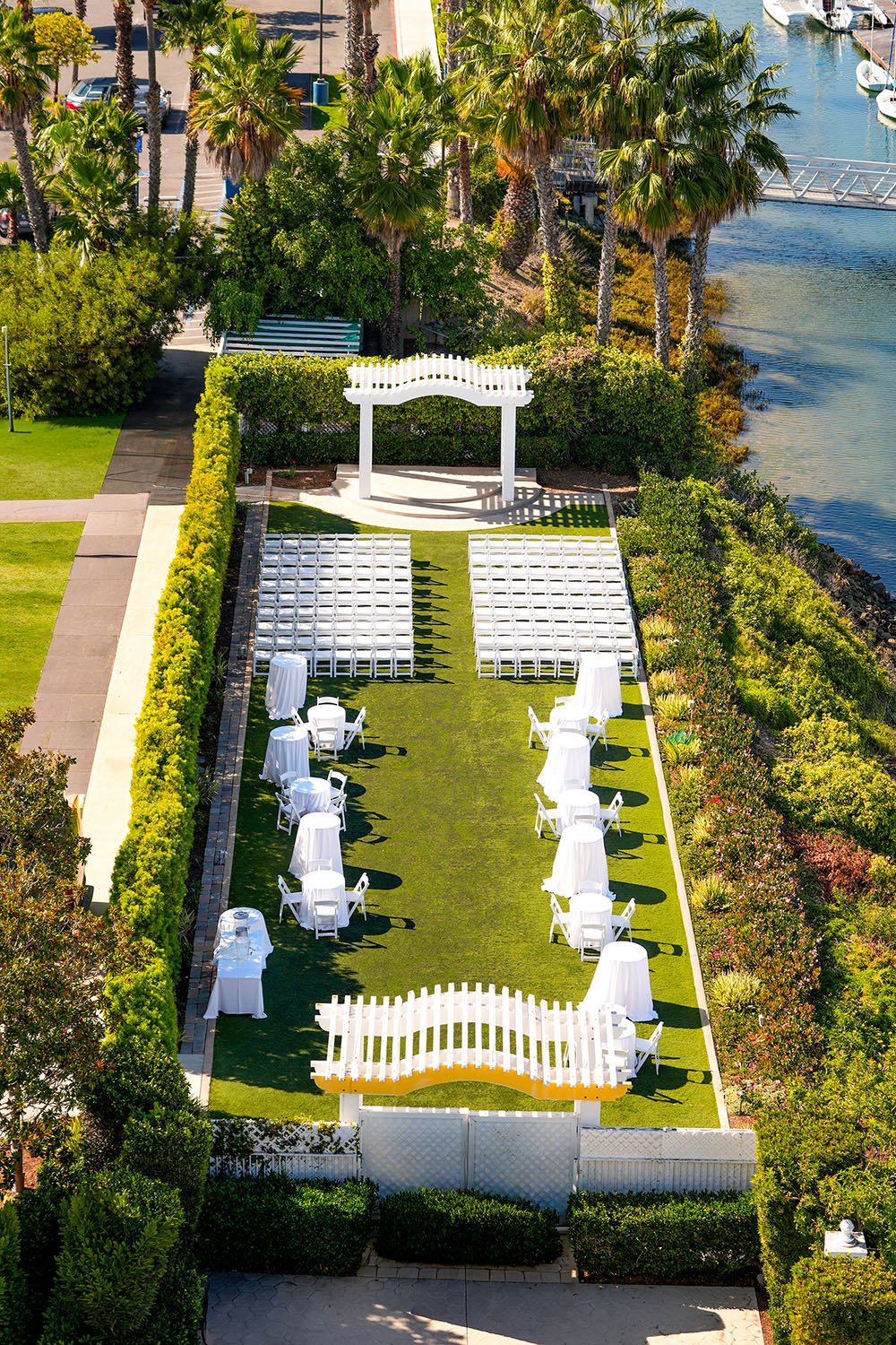 The venue is an oblong green area, bounded by well-maintained green hedges and a paved walkway. The ground cover appears to be artificial turf.