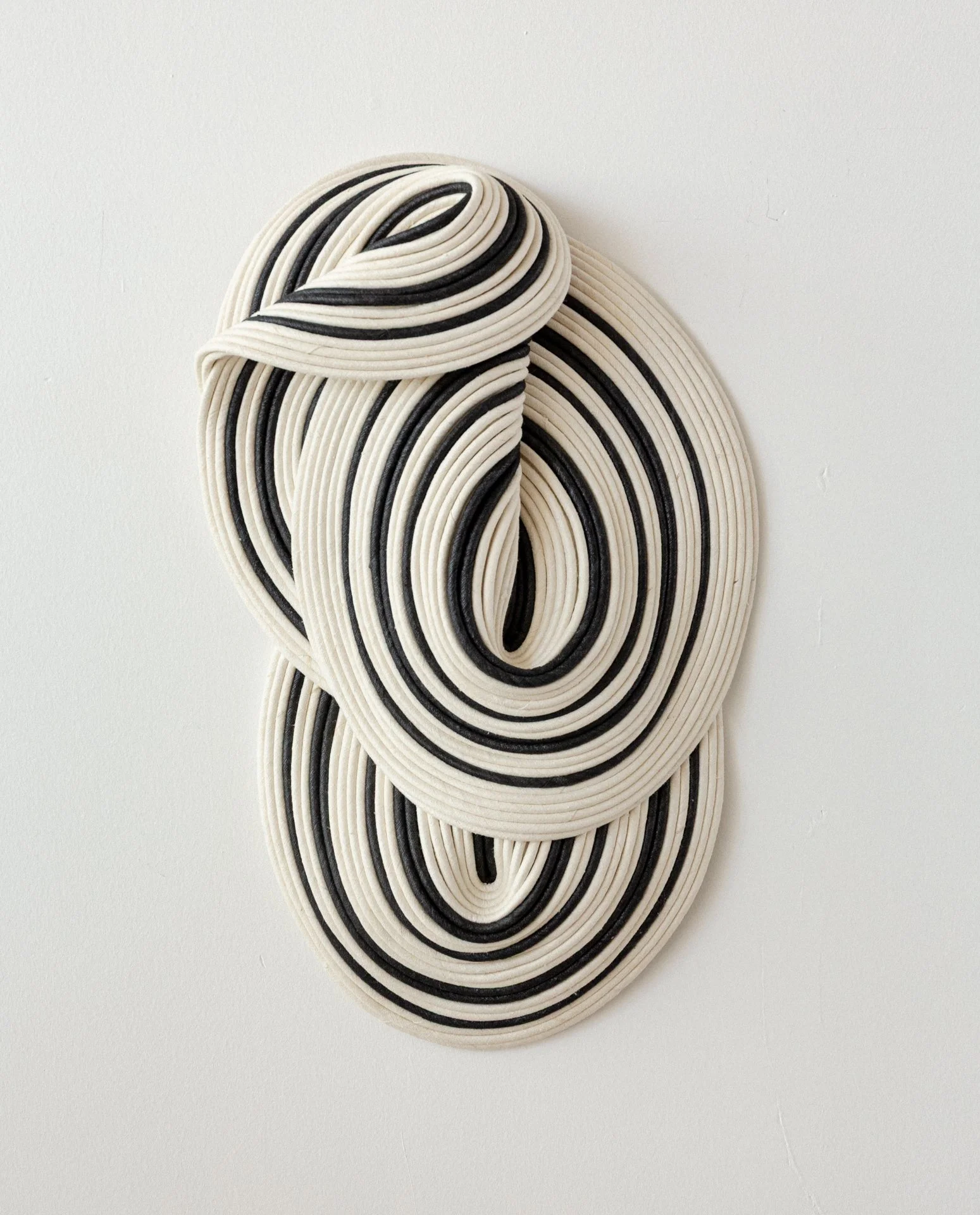 A piece of artwork consisting of black and white rubber tubing arranged in a coiled abstract pattern on a white background.