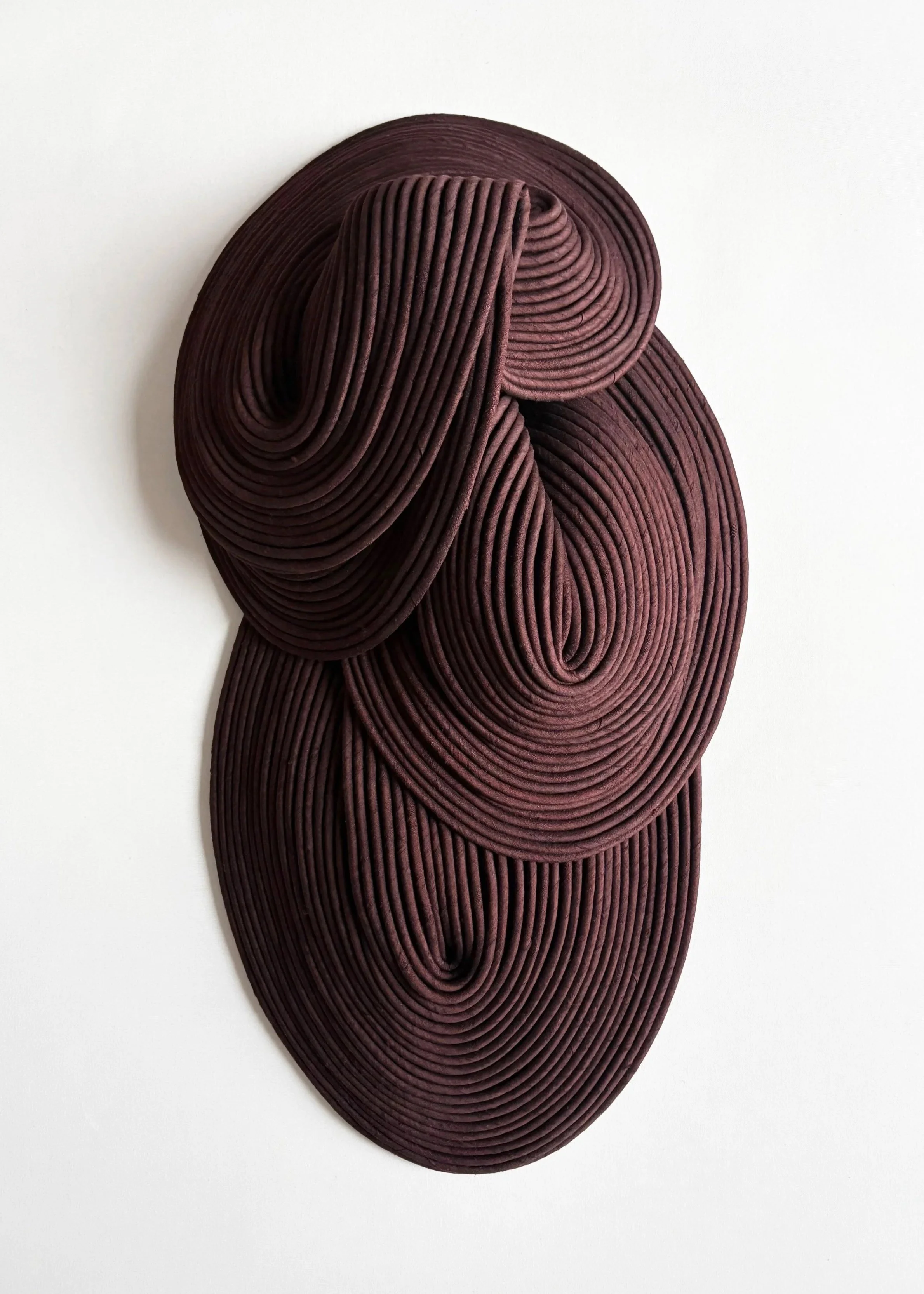 An abstract wall art piece made of layered, dark red, curved rubber or wood strips arranged in concentric, flowing shapes on a white background.