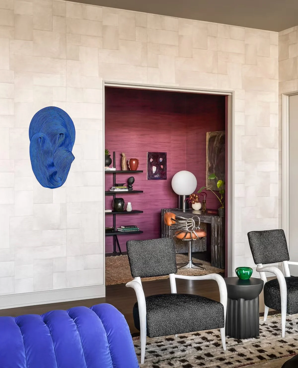 Living room with black and white chairs, a purple velvet sofa, a small black side table with a green kettle, and wall art including a blue wire sculpture of a human ear.