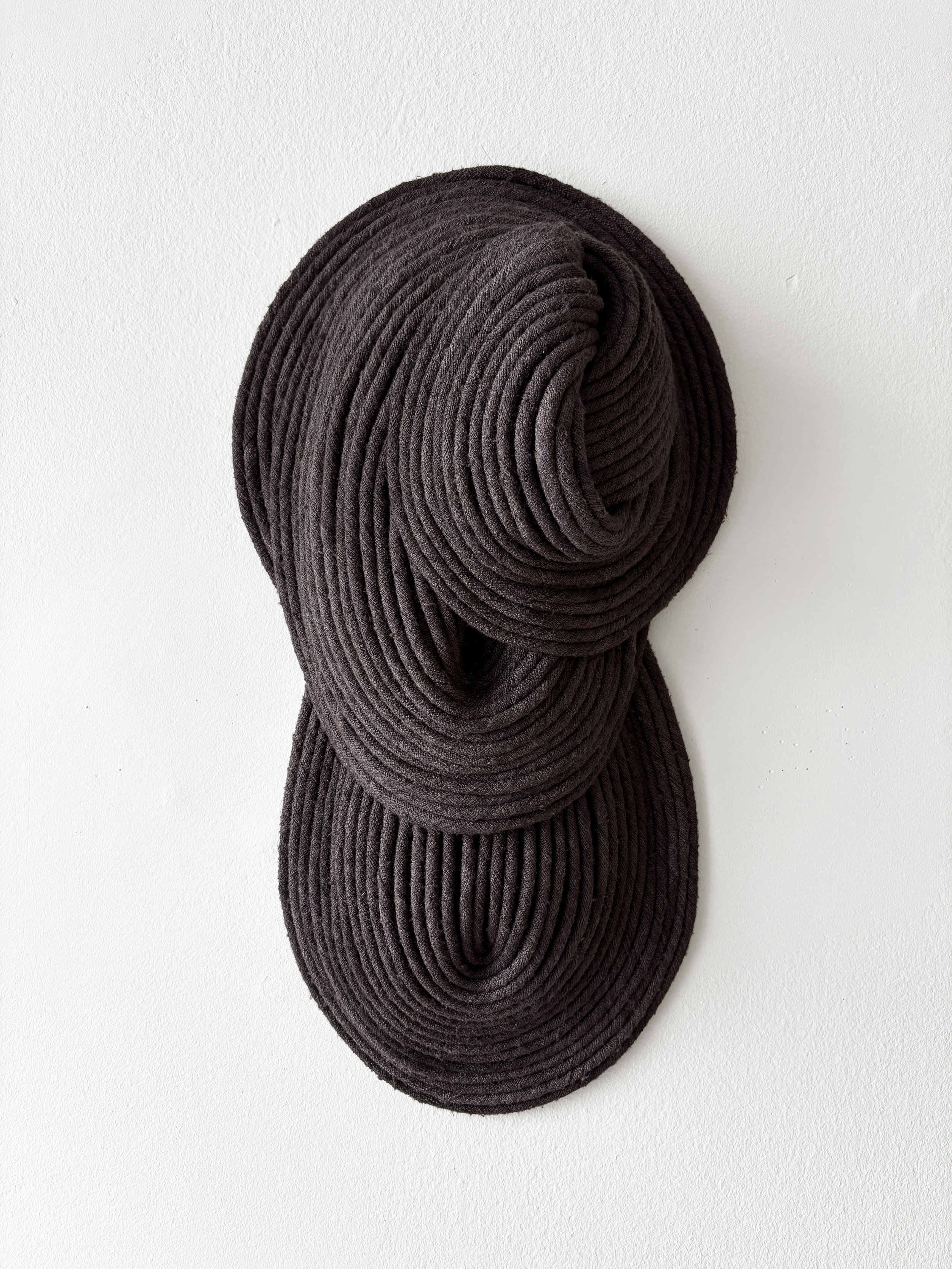 Three brown knitted coil-shaped head sculptures mounted on a white wall.