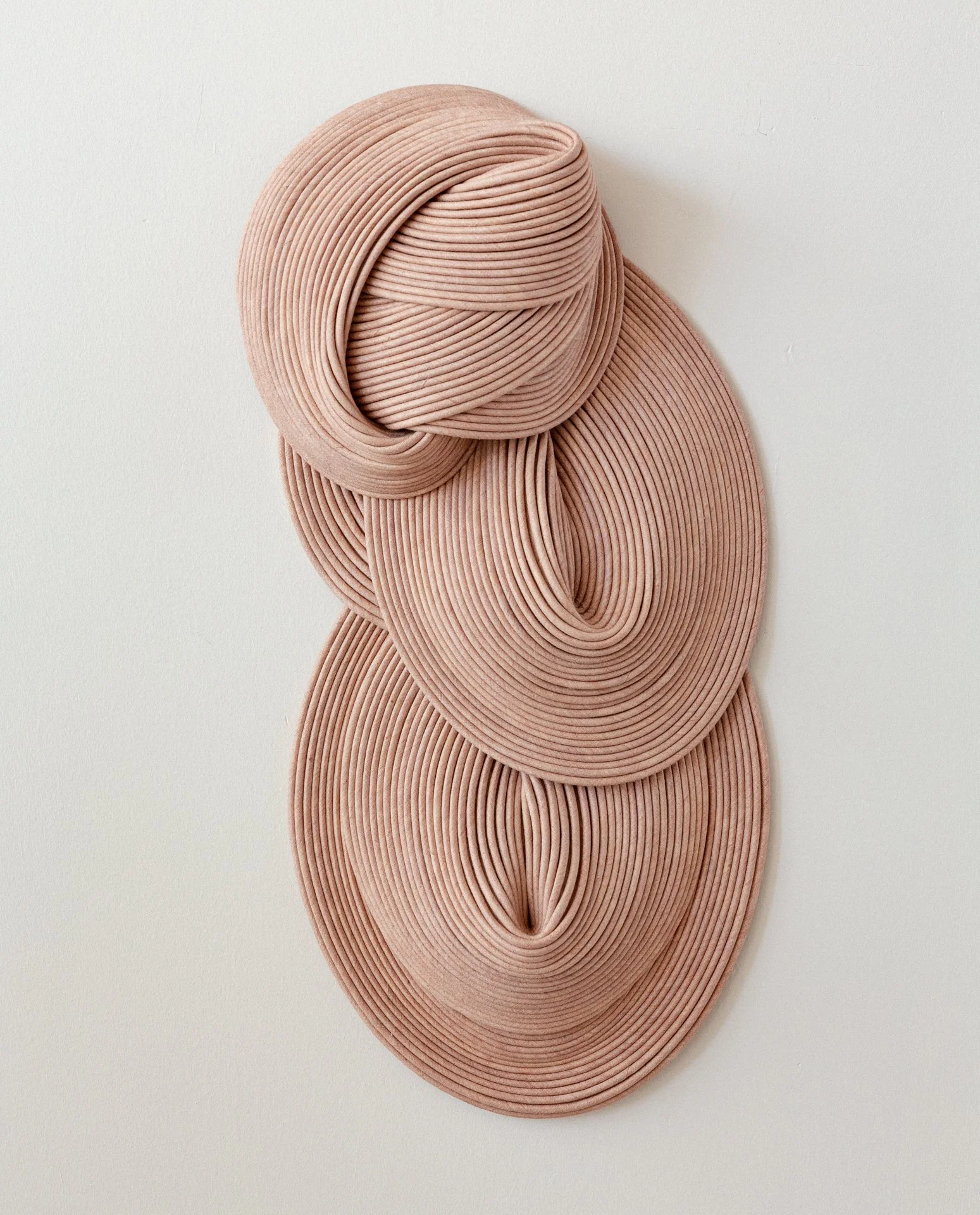 A wall art piece made of stacked and twisted pink rubber bands forming an abstract human figure on a white wall.