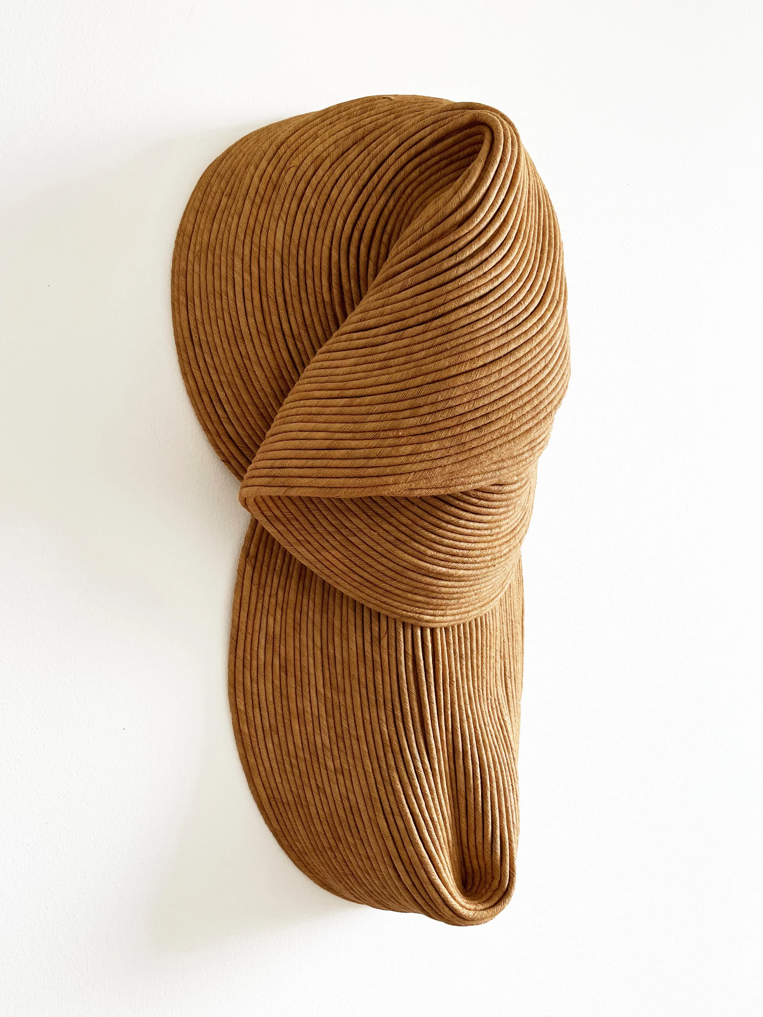 Close-up image of a folded, textured, ribbed fabric in a tan color, arranged in a flowing, layered pattern.