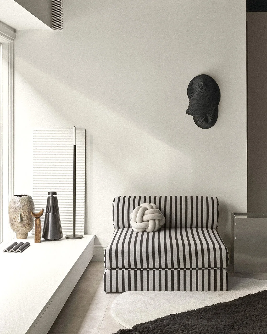 A modern living room corner with a black and white striped sofa, a knotted white cushion, decorative vases on a white ledge, and two black hats hanging on the white wall.