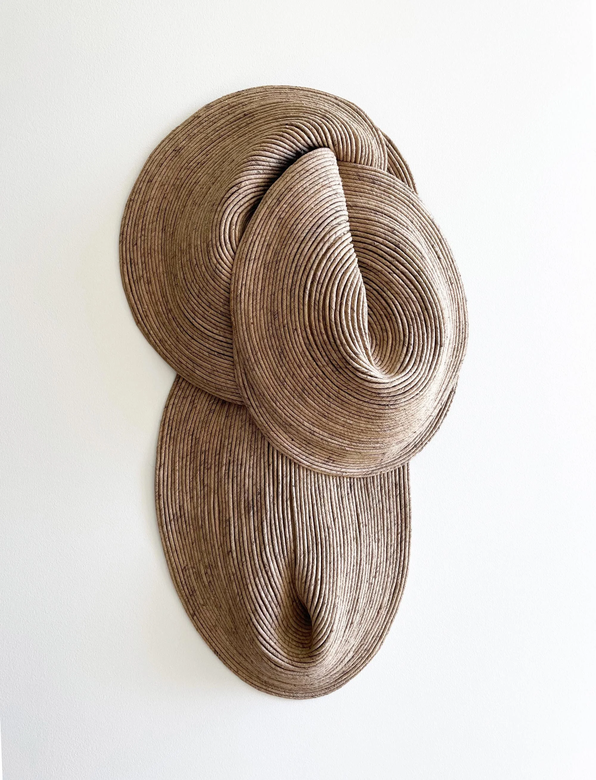 Three layered, circular, wooden sculptures arranged vertically on a white wall.