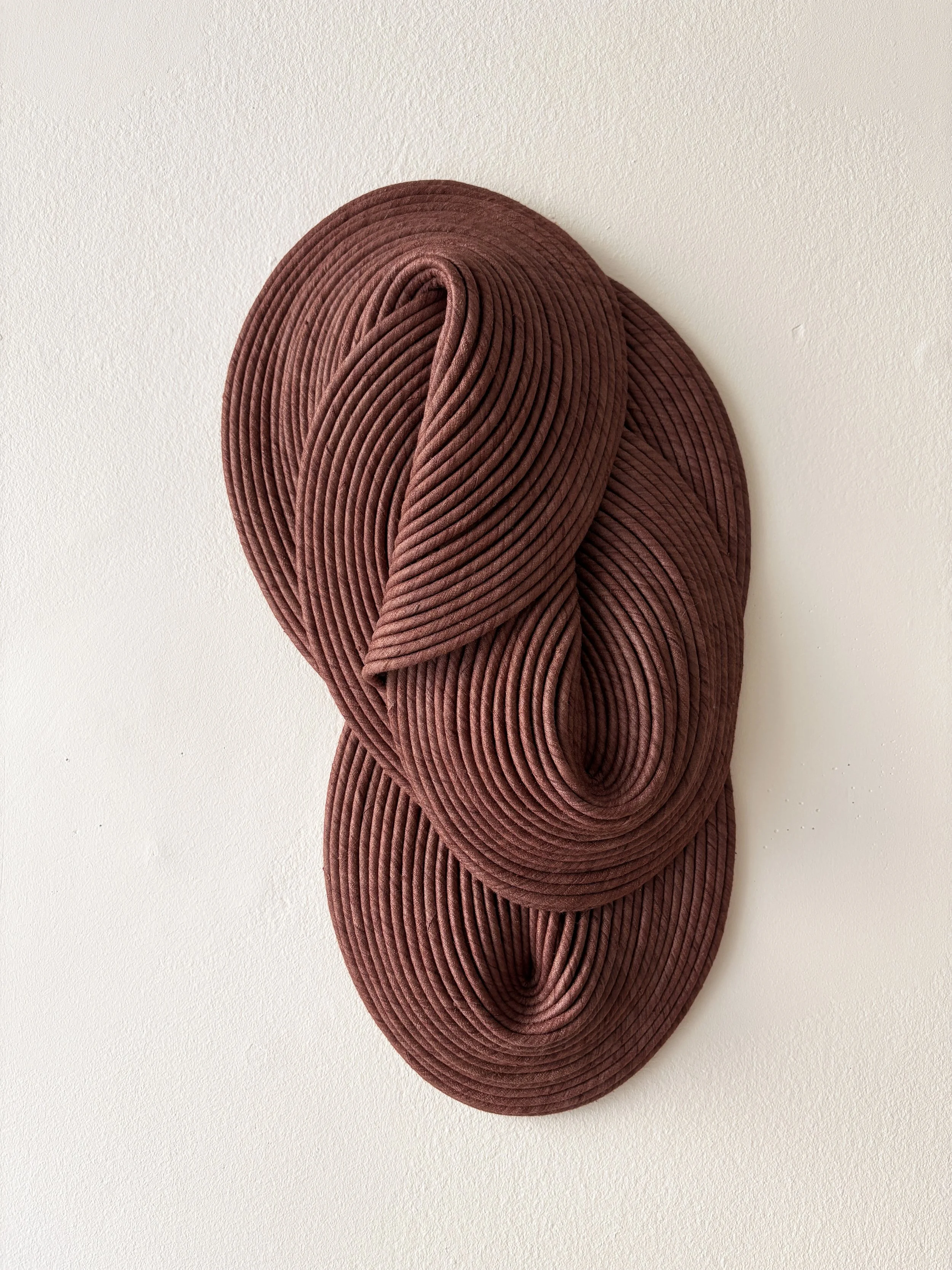 A large, decorative, 3D art piece made of concentric pinkish-burgundy velvet cords mounted on a white wall.