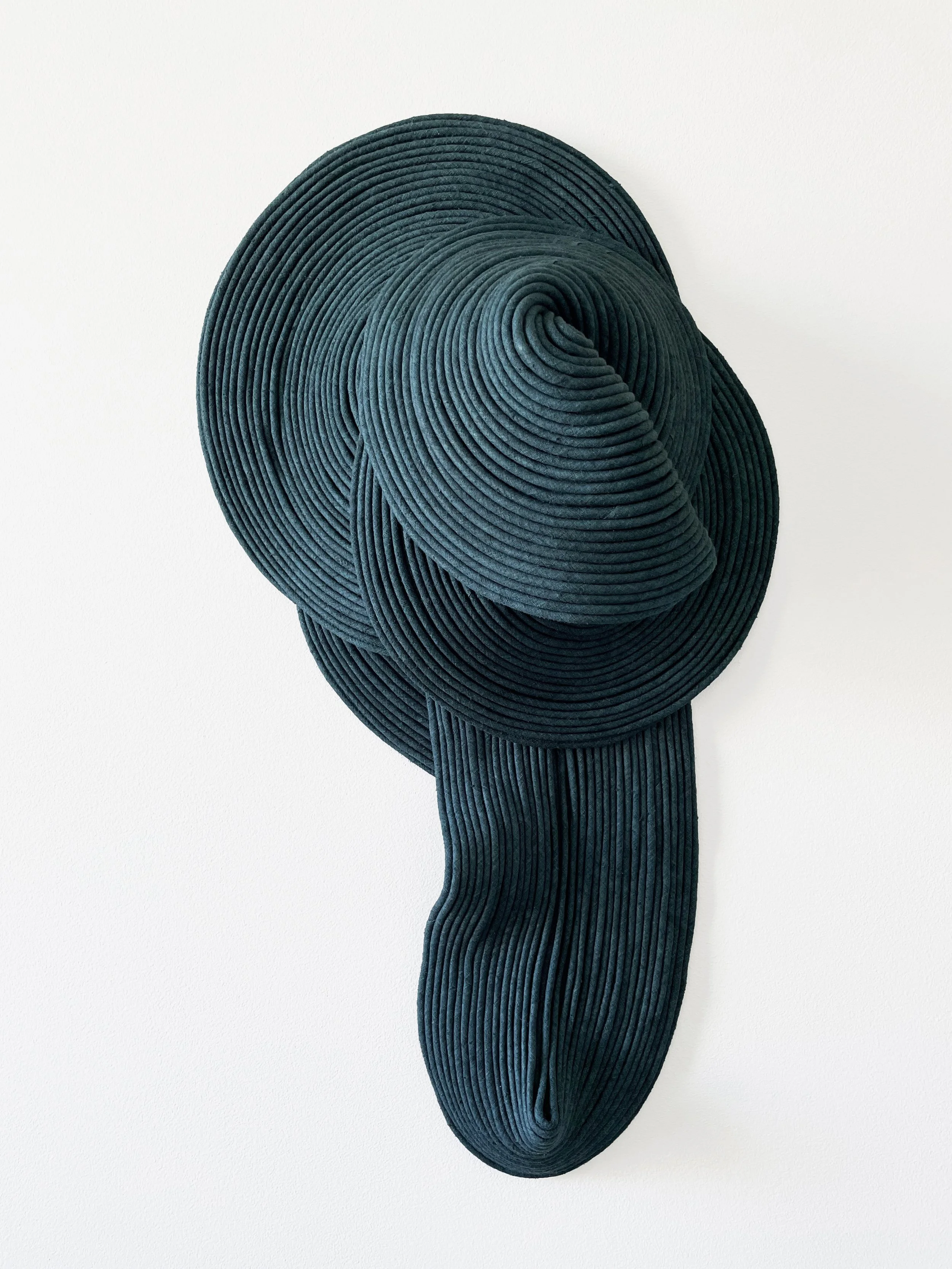 A wall art piece made of layered black banding arranged in a spiral pattern, creating a three-dimensional abstract shape on a white wall.