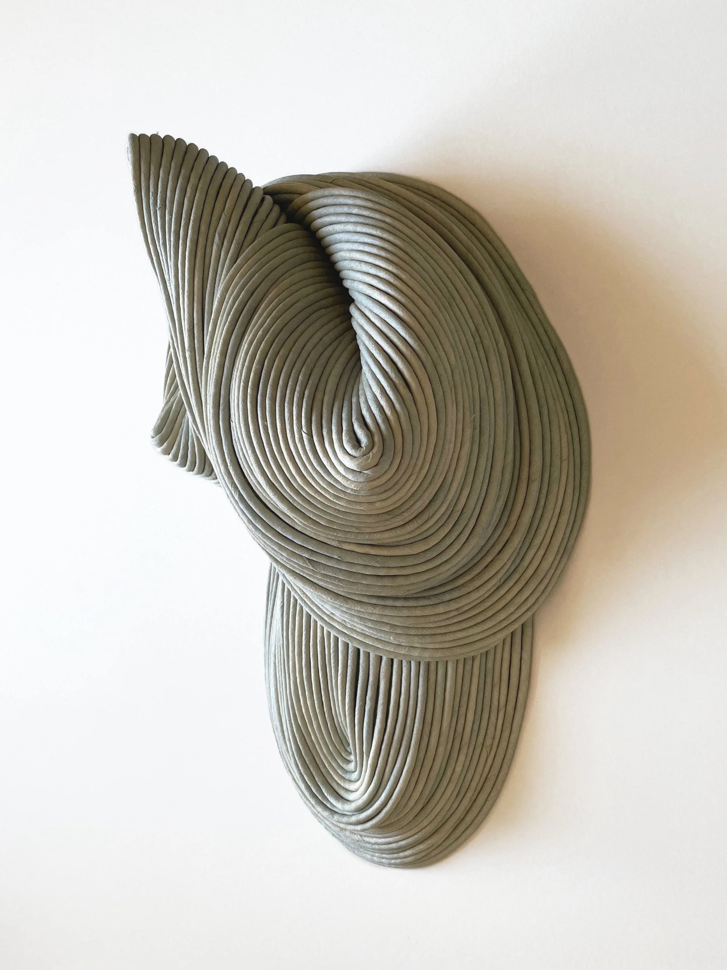 A three-dimensional abstract sculpture made of stacked, layered, curved gray shapes forming a complex, artistic design.