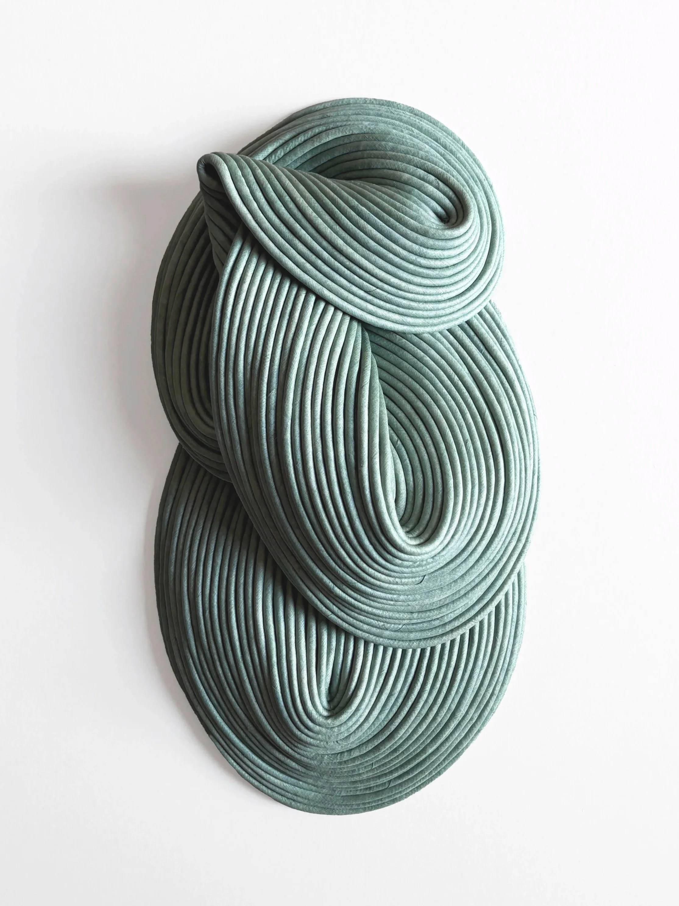 Three identical large, green, fabric-covered, coiled, and twisted sculptures mounted on a plain white wall.