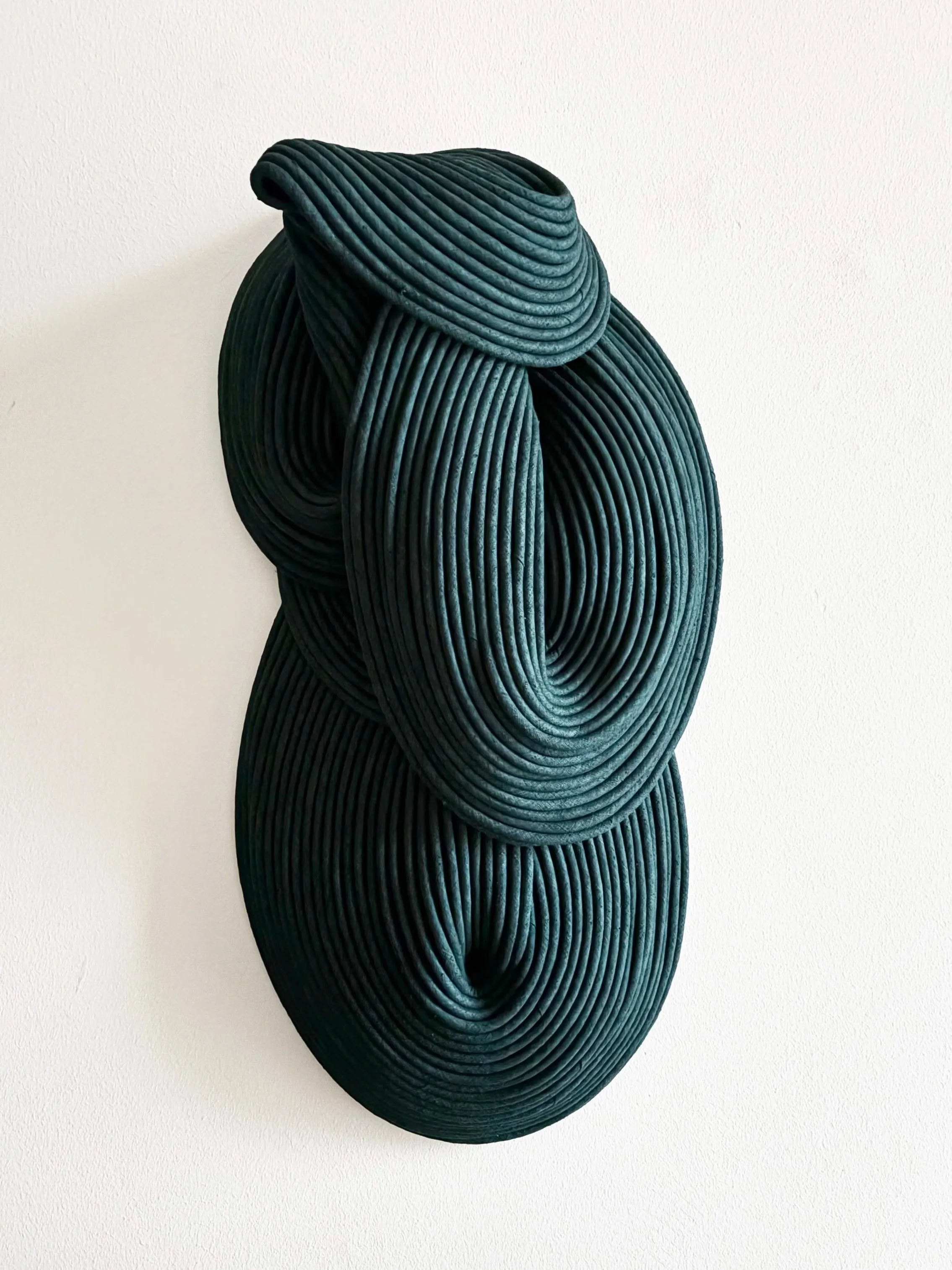 Abstract modern wall sculpture made of concentric black loops on white wall.