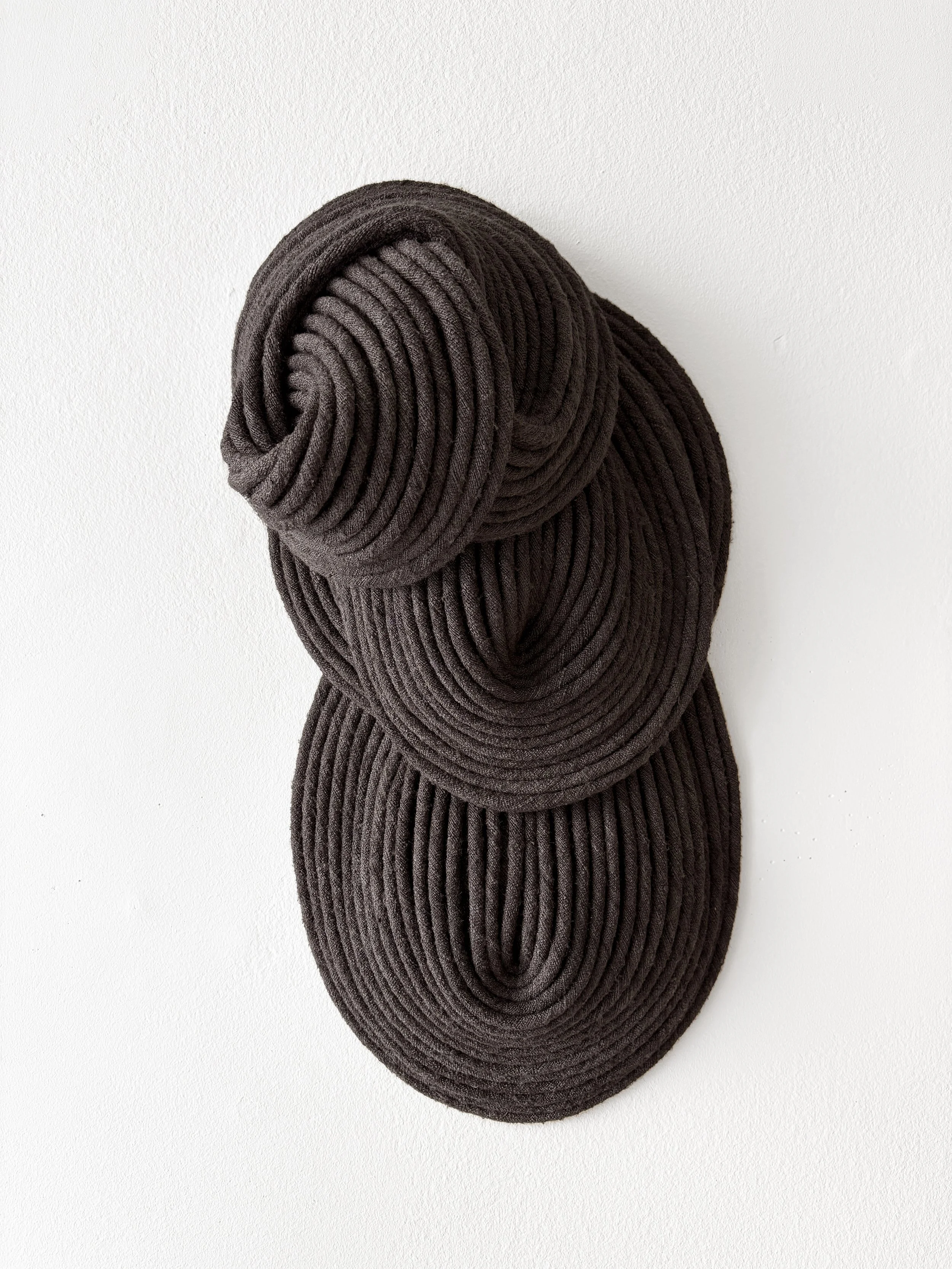 A set of four dark brown, ribbed, fabric-covered objects stacked against a white wall.