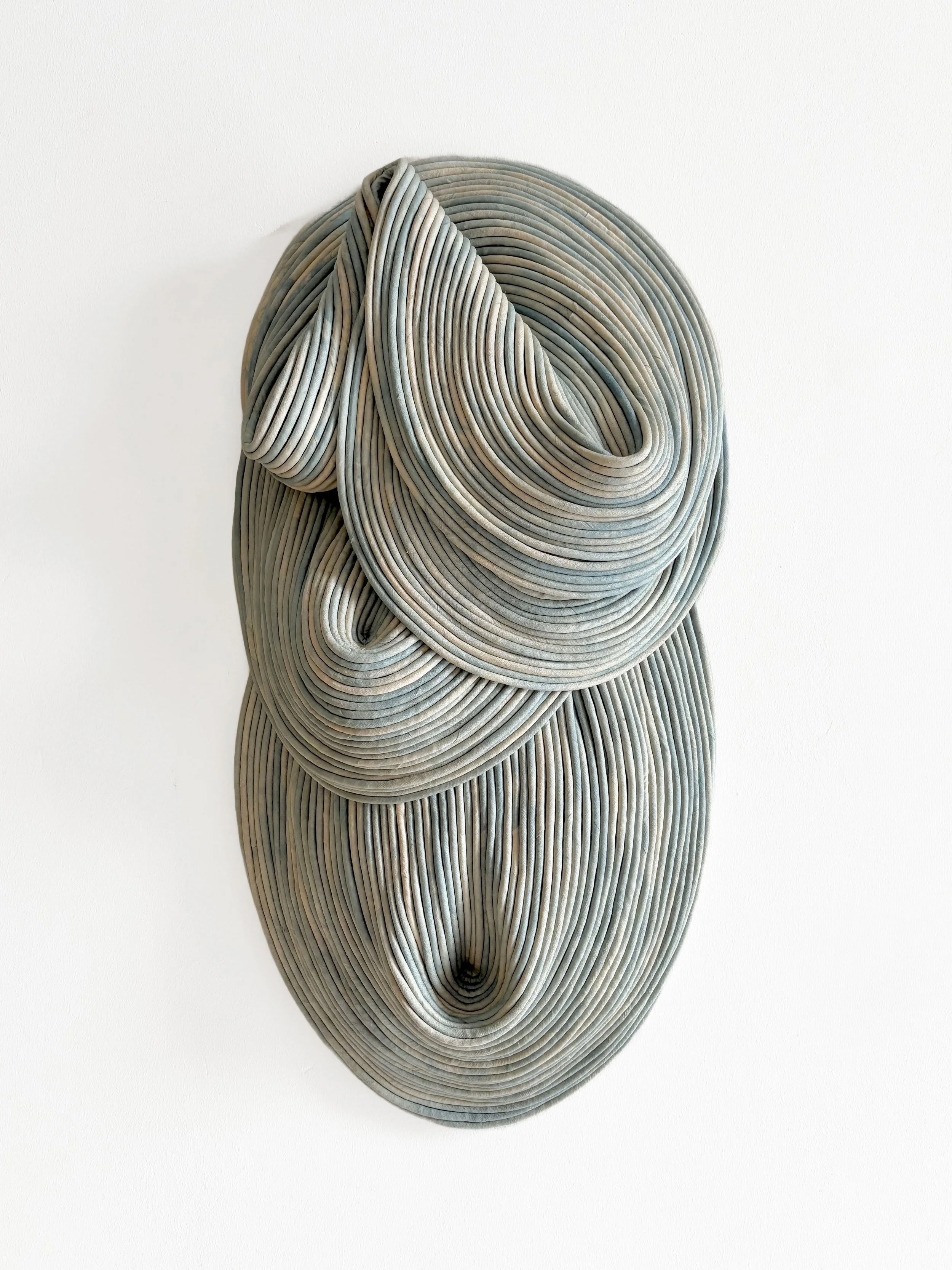 Abstract wall sculpture made of layered, curved strips of material forming organic, flowing shapes in neutral tones.
