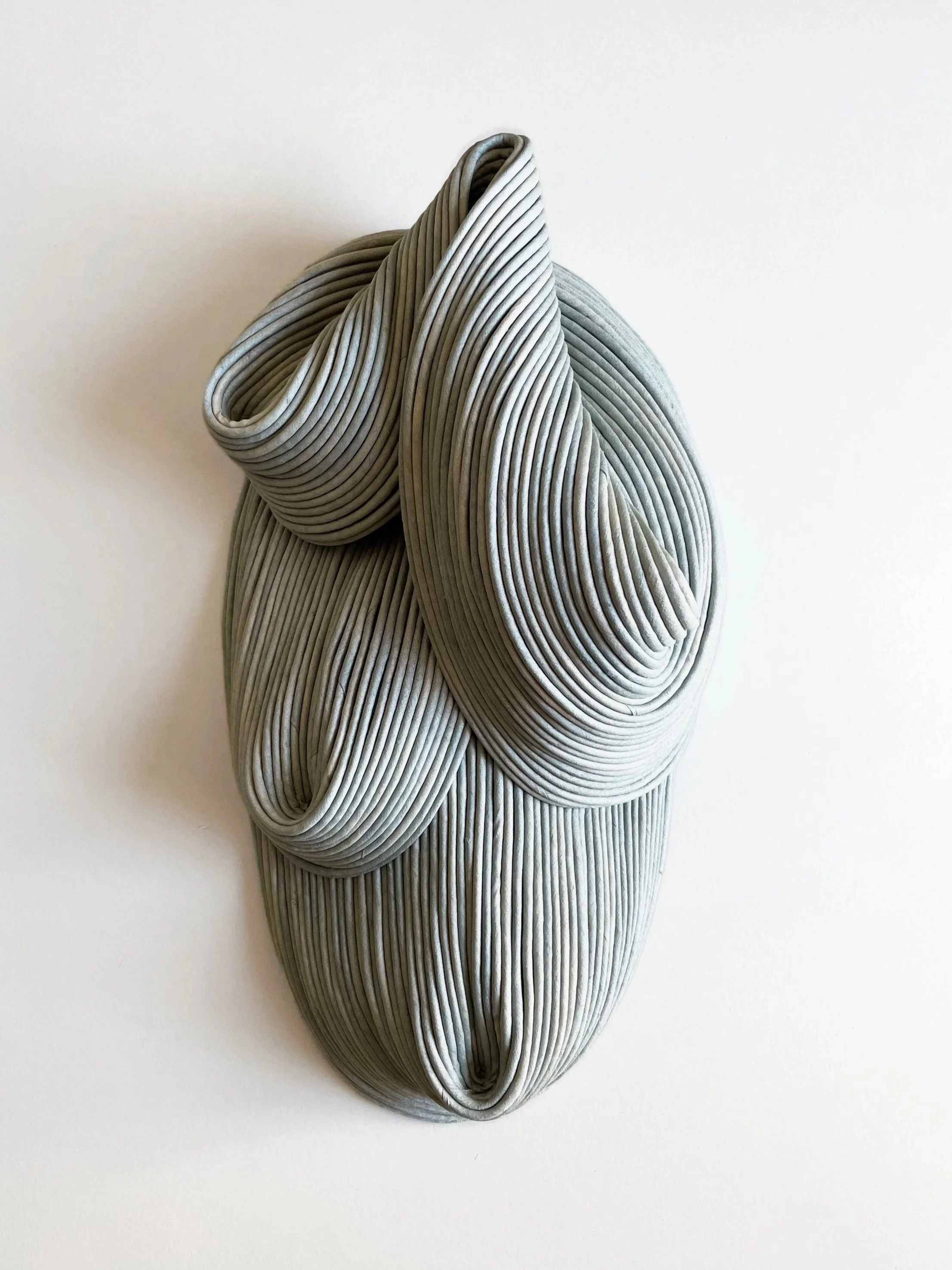 A modern, abstract sculpture made of layered, curved, grayish material with intricate folds and a textured appearance.
