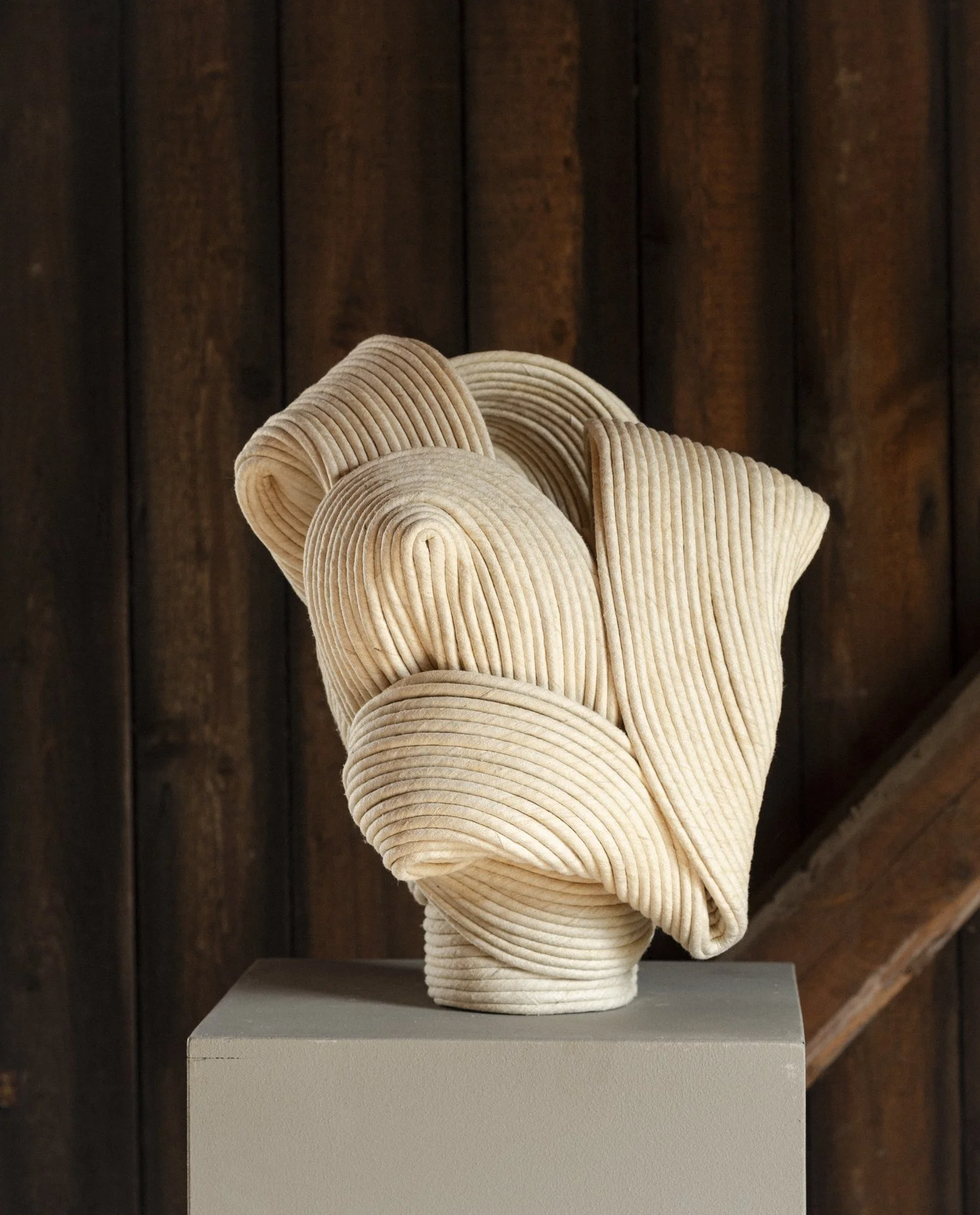 Ceramic sculpture resembling a human head with ridged, textured surface against wooden background.