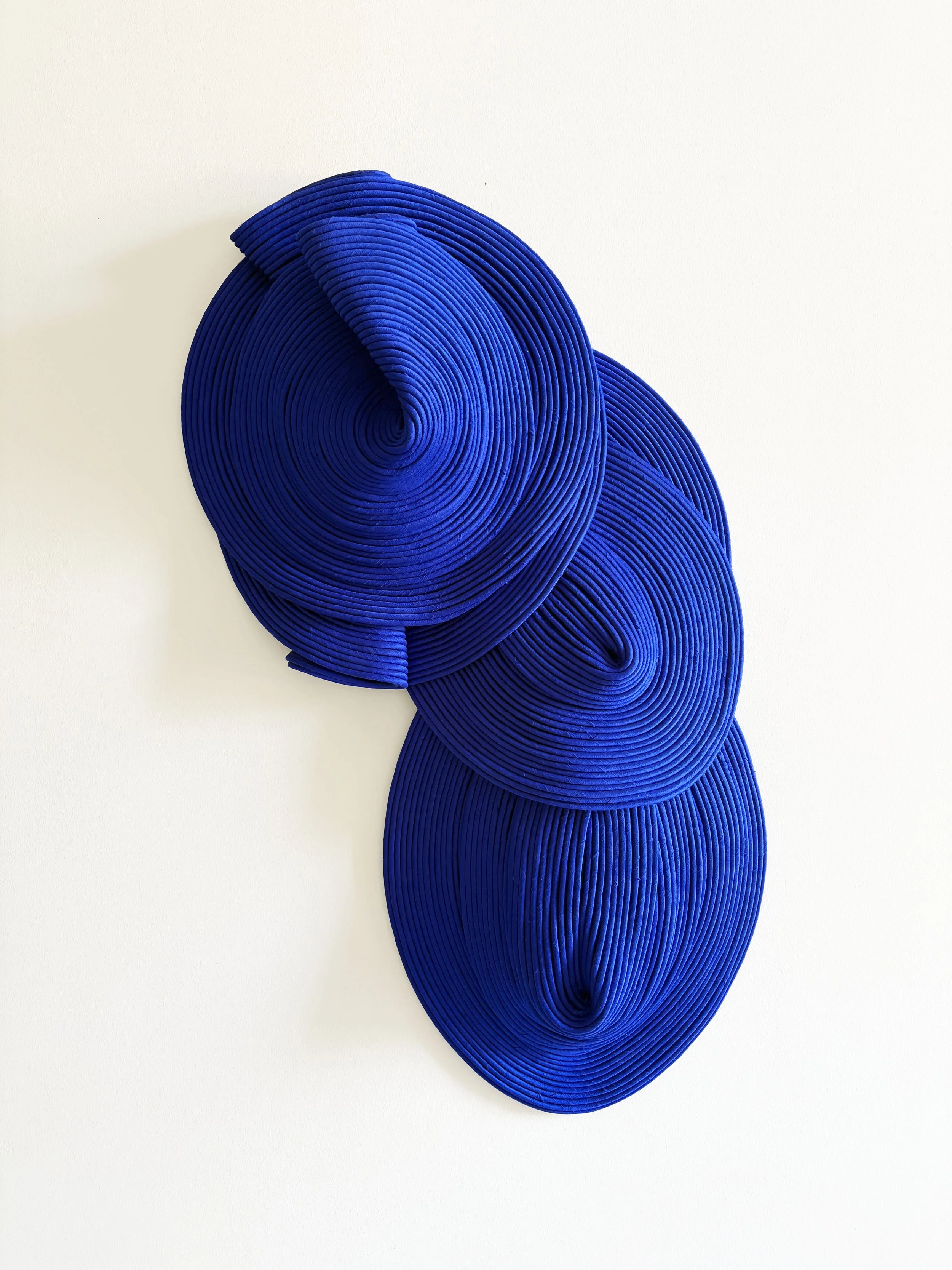 Three layered blue spiral sculptures mounted on a white wall.