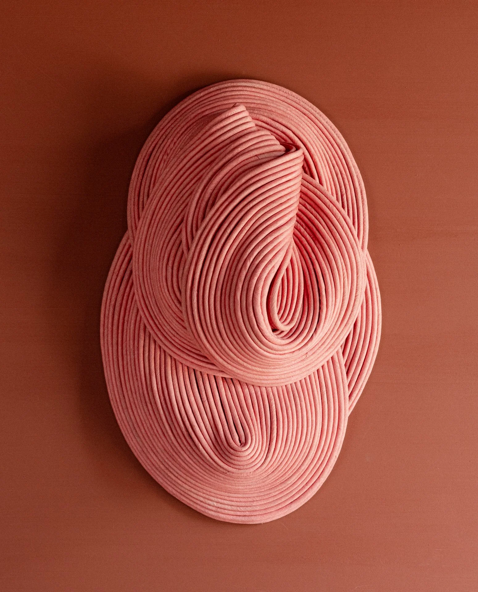 Pink coiled cord arranged on a flat surface resembling a human face with closed eyes and a nose.