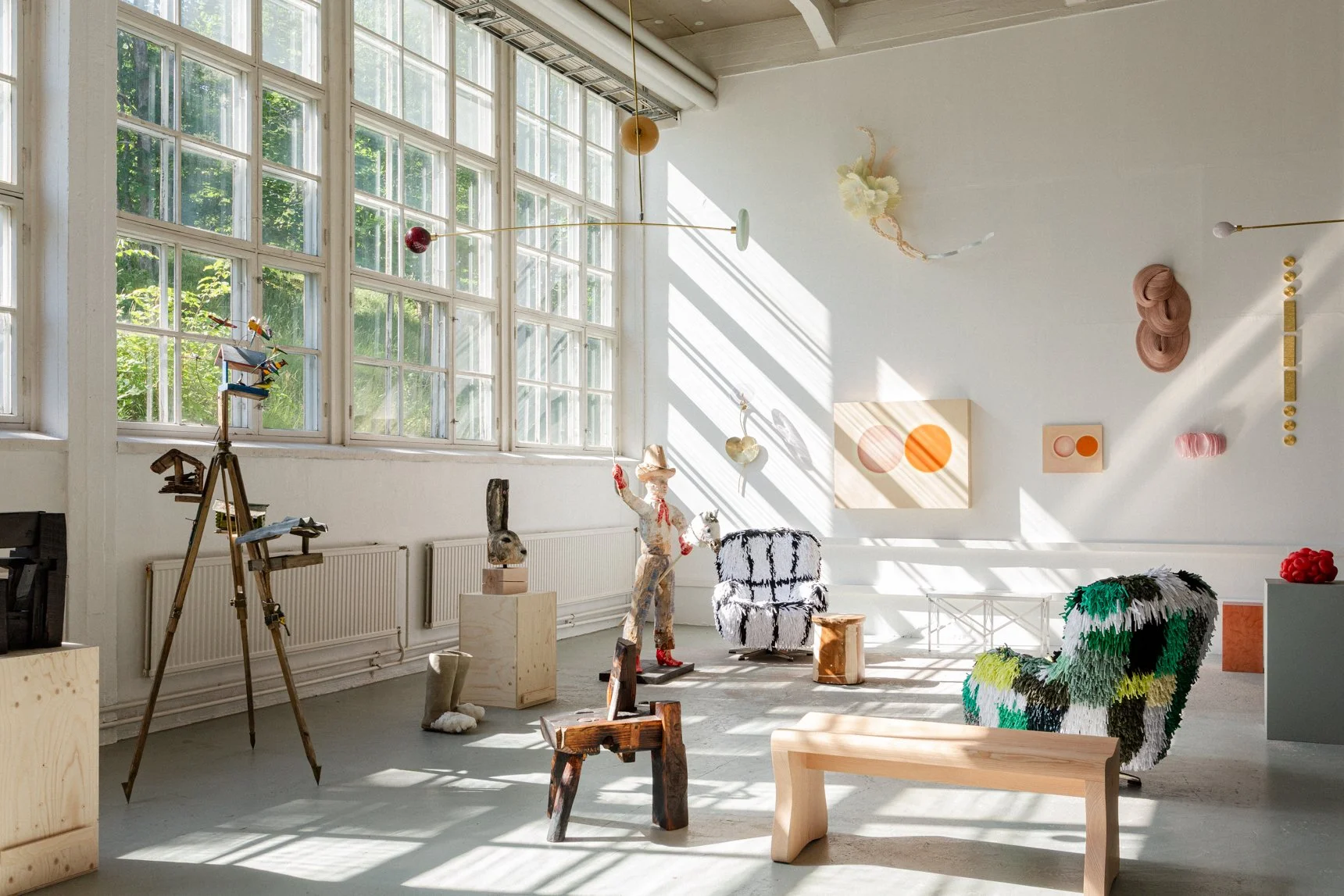 An art gallery with sculptures and wall art, illuminated by natural sunlight through large window panes.