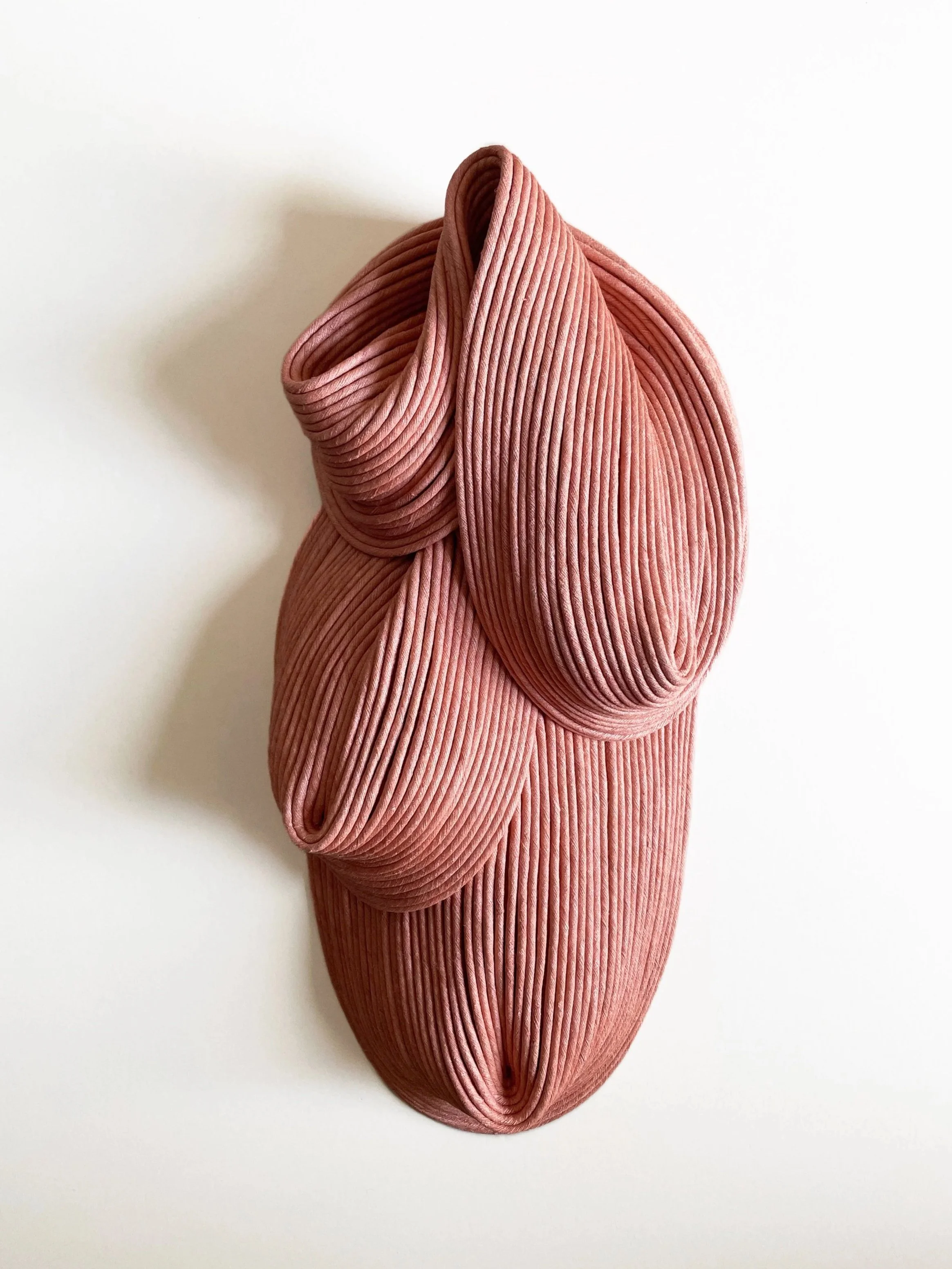 A pink, ribbed fabric sculpture resembling an abstract, three-dimensional form with flowing, layered folds.