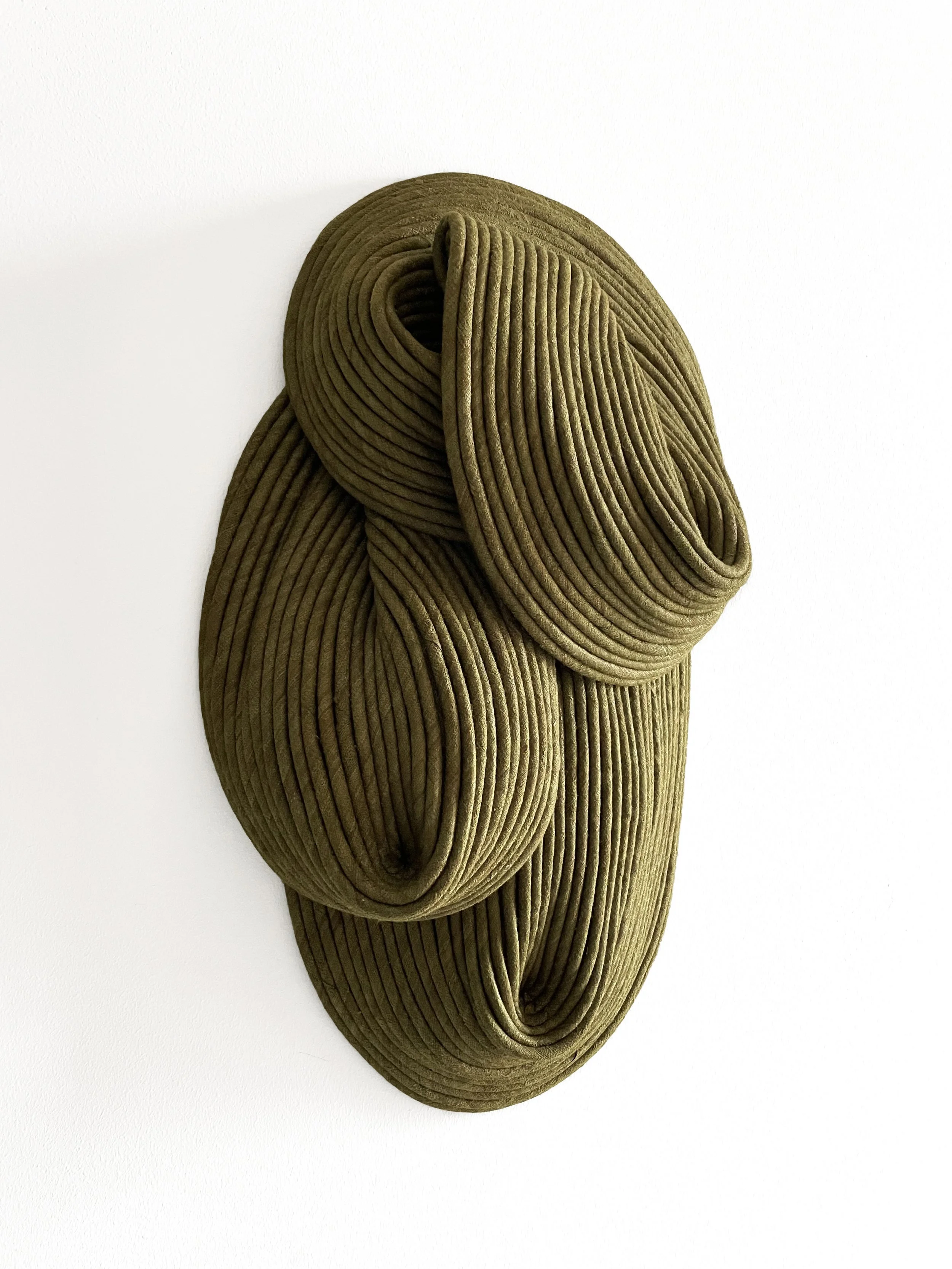 A piece of contemporary wall art made from tightly coiled green velvet fabric, arranged in an abstract, flowing shape on a white background.
