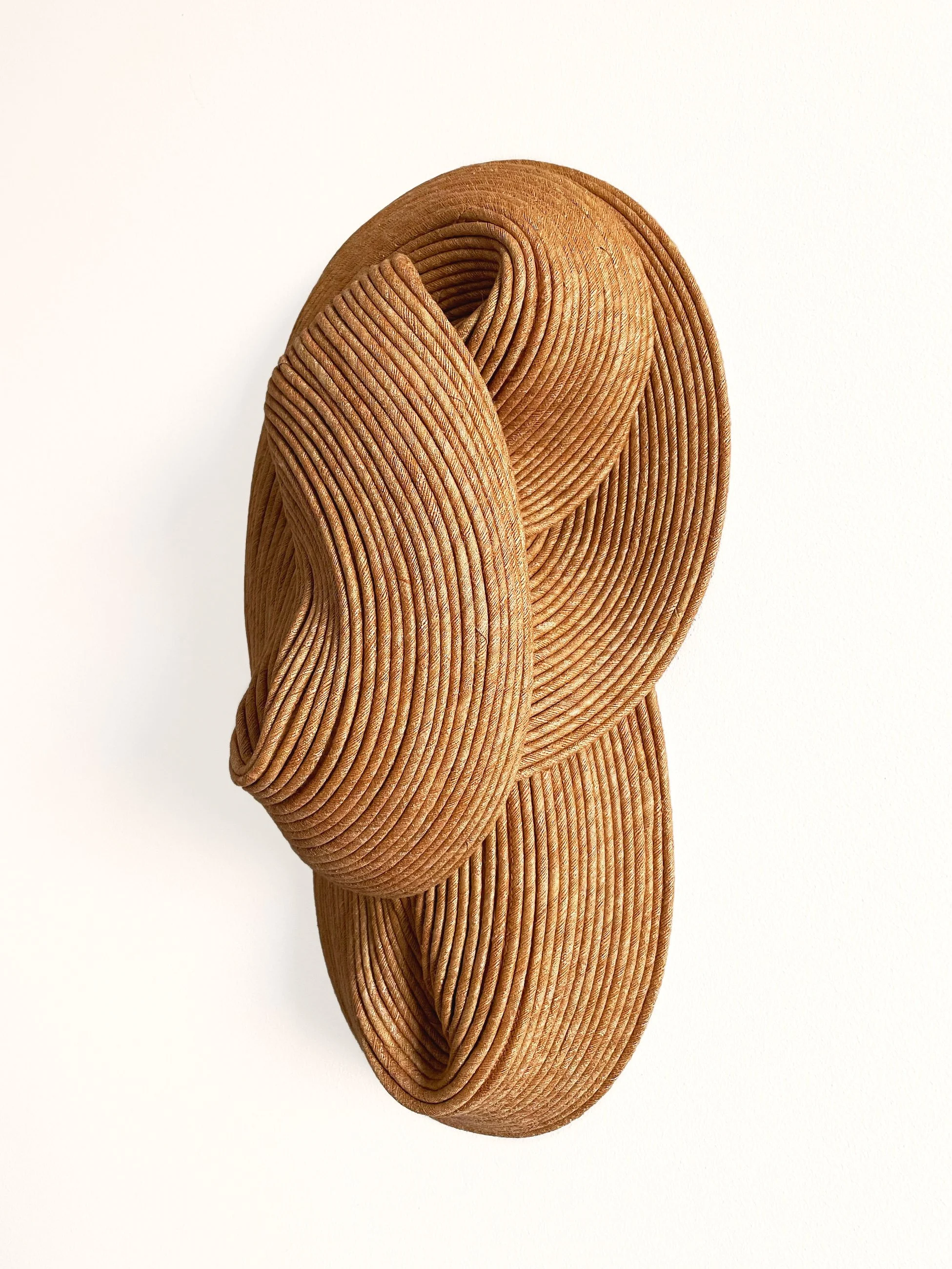 A modern, abstract sculpture composed of curled, ribbon-like wooden strips arranged in a layered, flowing form against a plain white background.