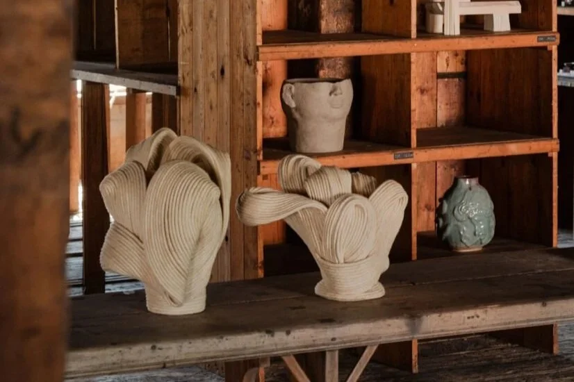 Two handmade ceramic vases with abstract designs on a wooden shelf in a rustic setting.
