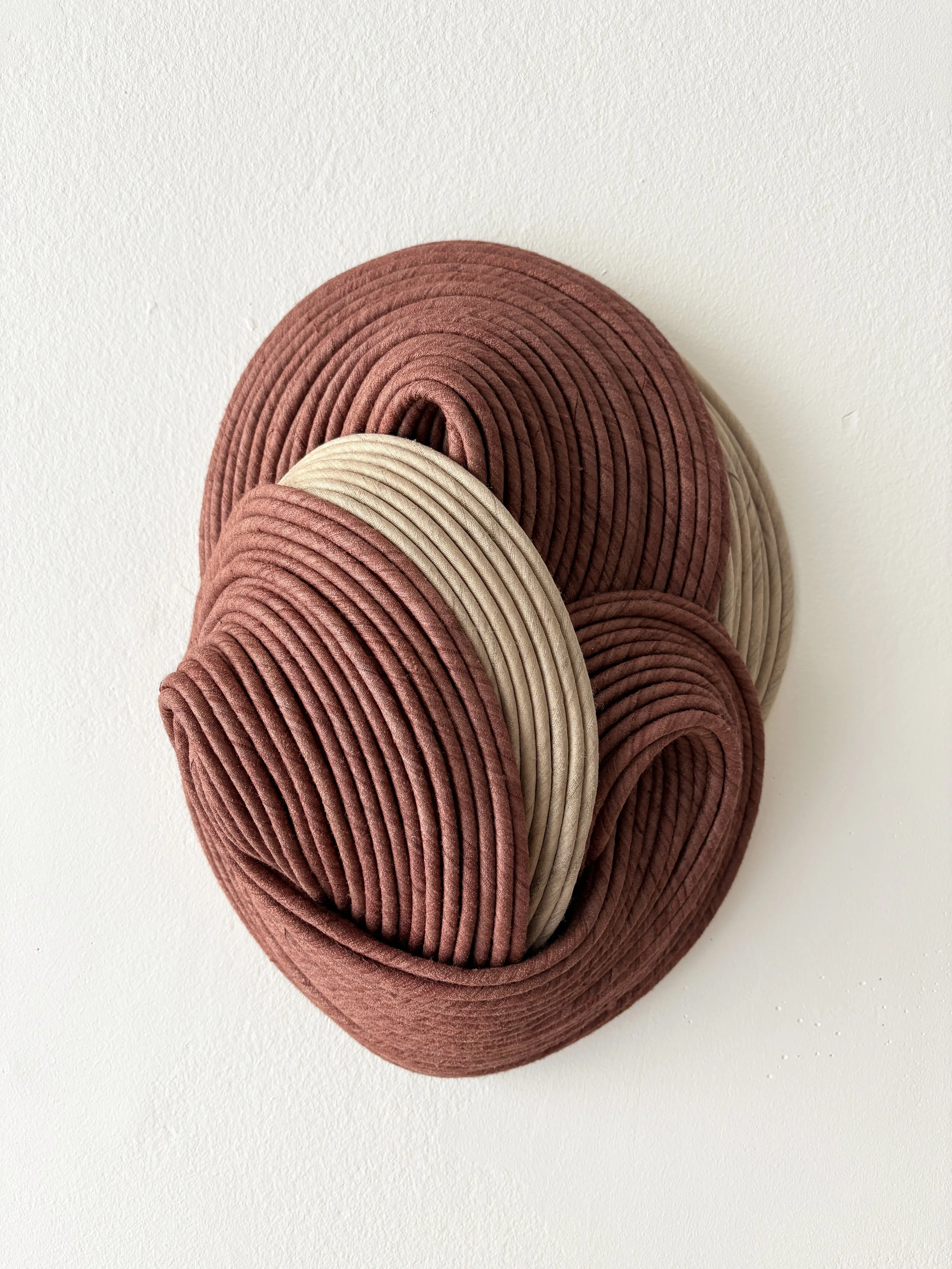 Decorative wall art made of multiple loops of pink and beige cord arranged in a circular pattern on a white wall.